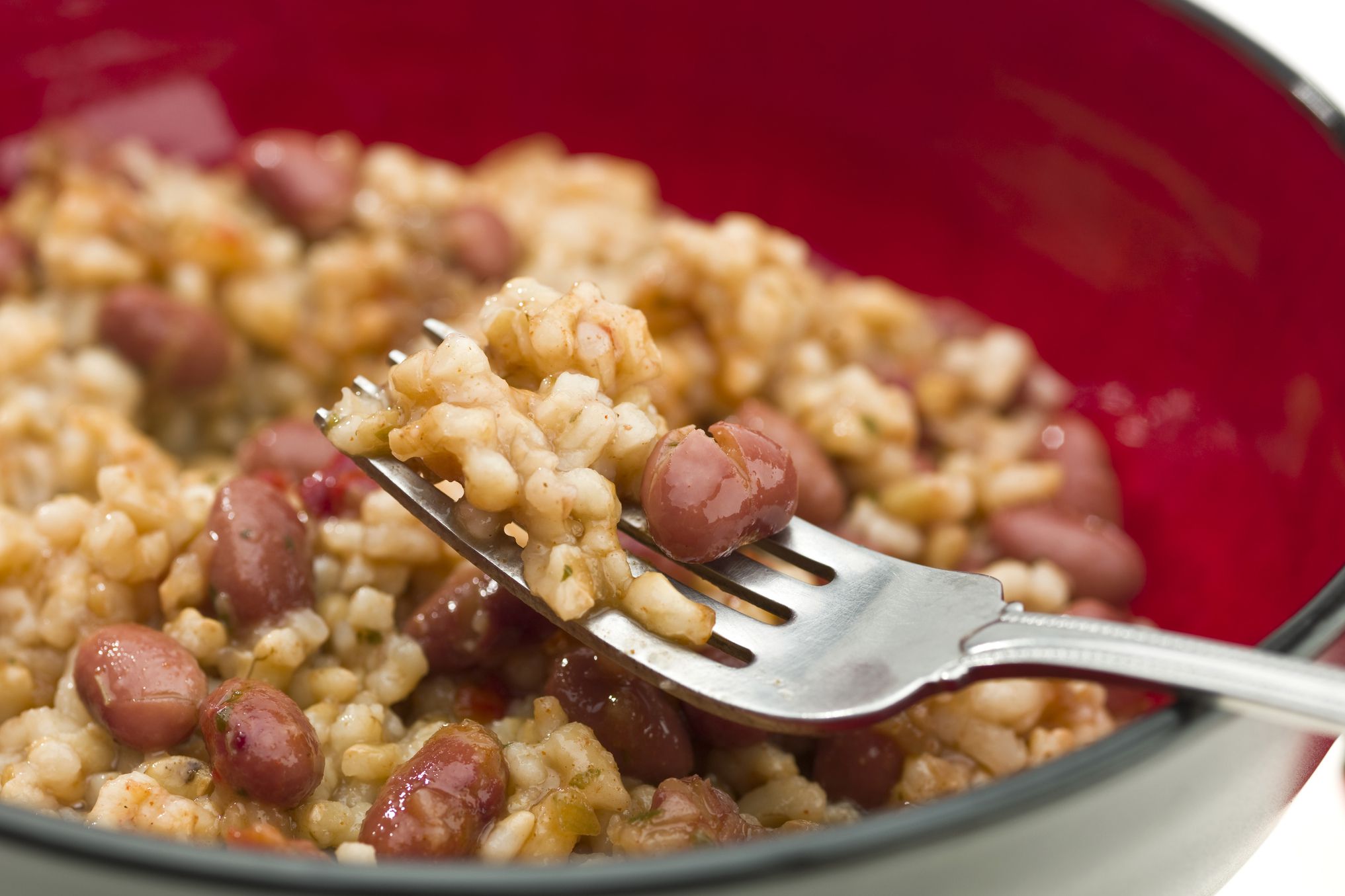 Closeup of instant pot rice and beans in a black with red inside bowl with a fork holding a portion