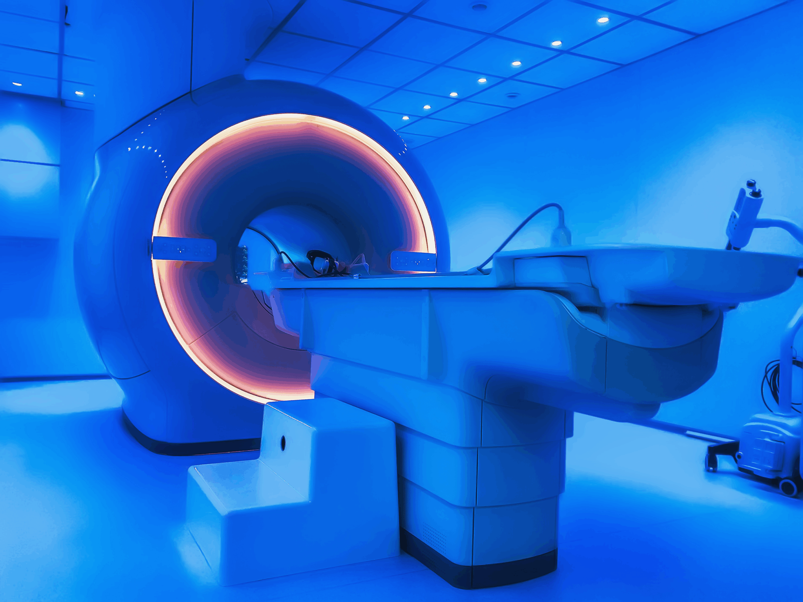 A magnetic resonance tomography imaging scanning device (MRI) in a hospital room, blue light in the room, clean and modern room