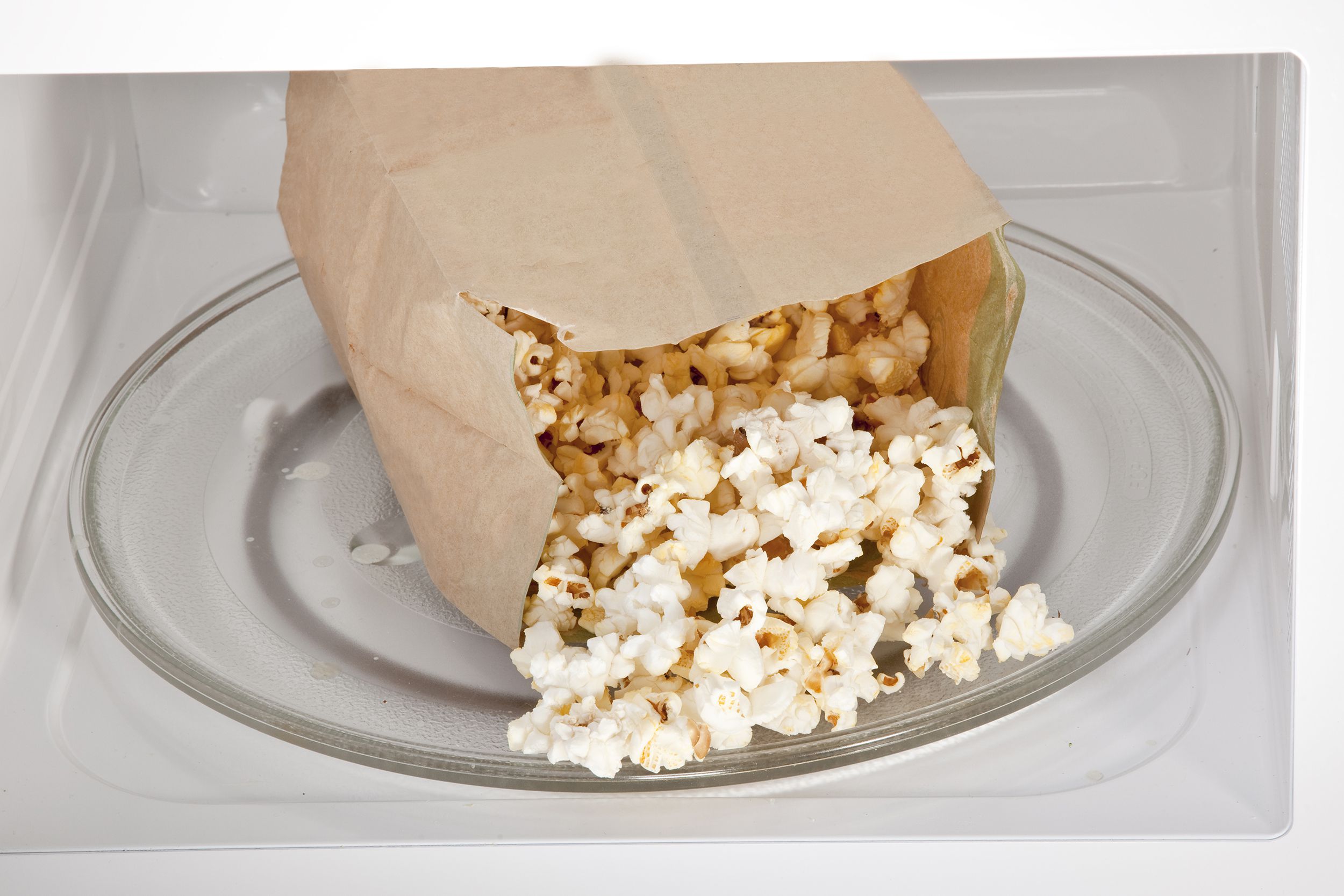 Opened bag of cooked popcorn on the glass turntable plate in a clean white microwave