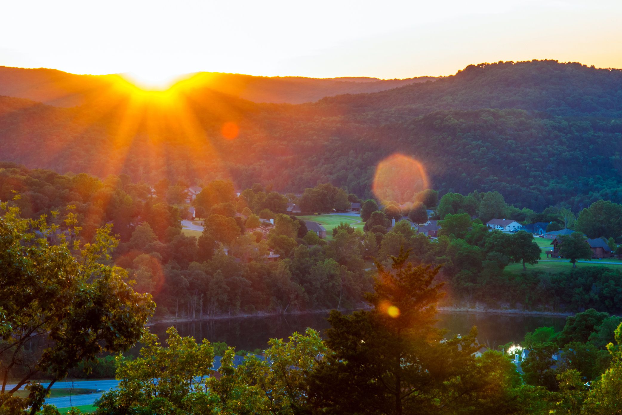 Ozark Mountains of Eureka Springs, Arkansas, during sunset, dramatic display of light in the image in the top left, homes in the foreground in the hills