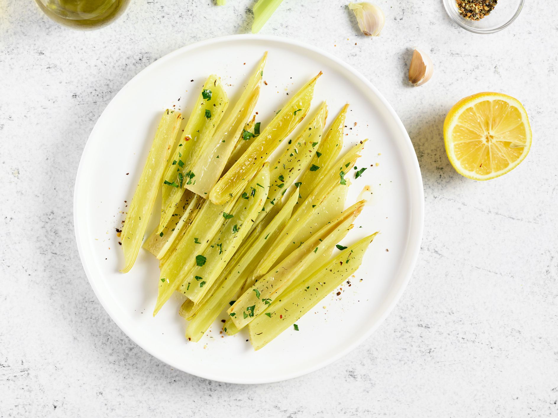 Braised celery on plate over light stone background. Top view, flat lay