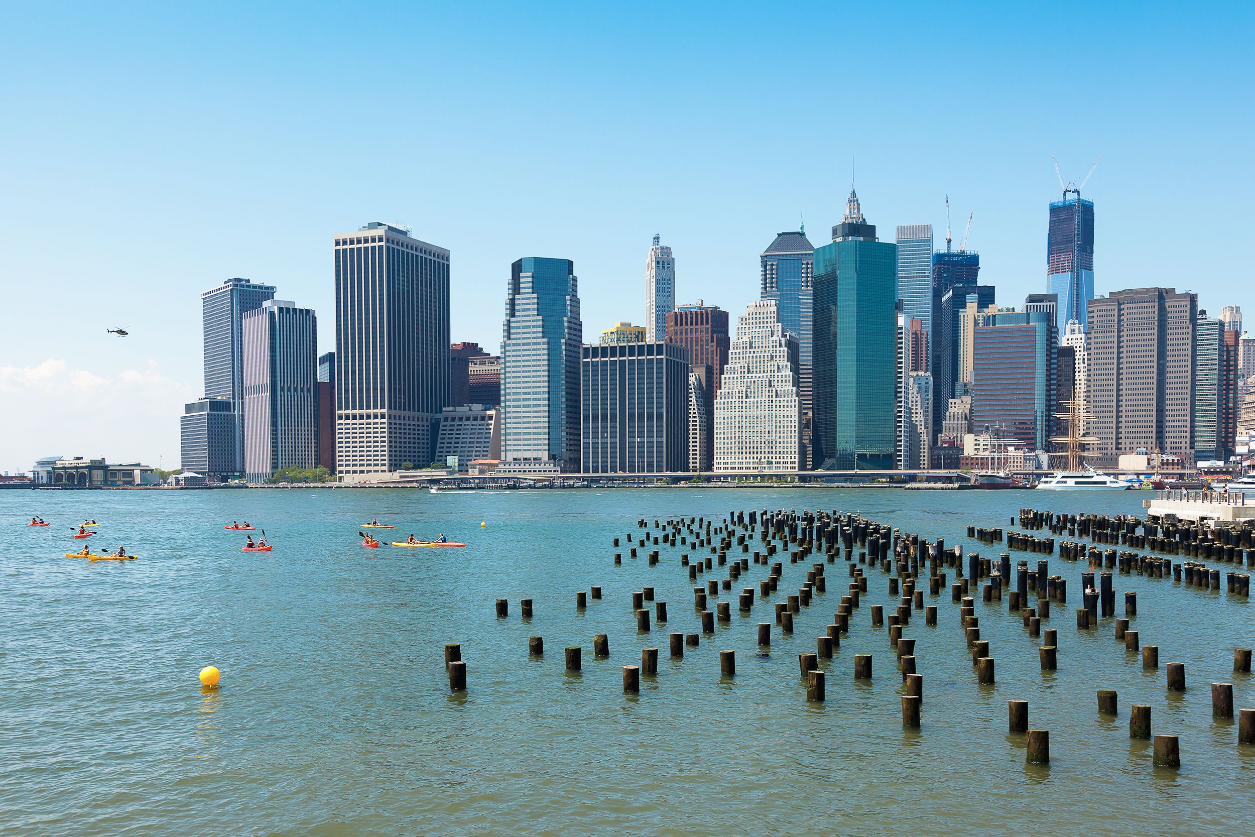 People kayaking in the river with lower Manhattan in the background on a sunny day