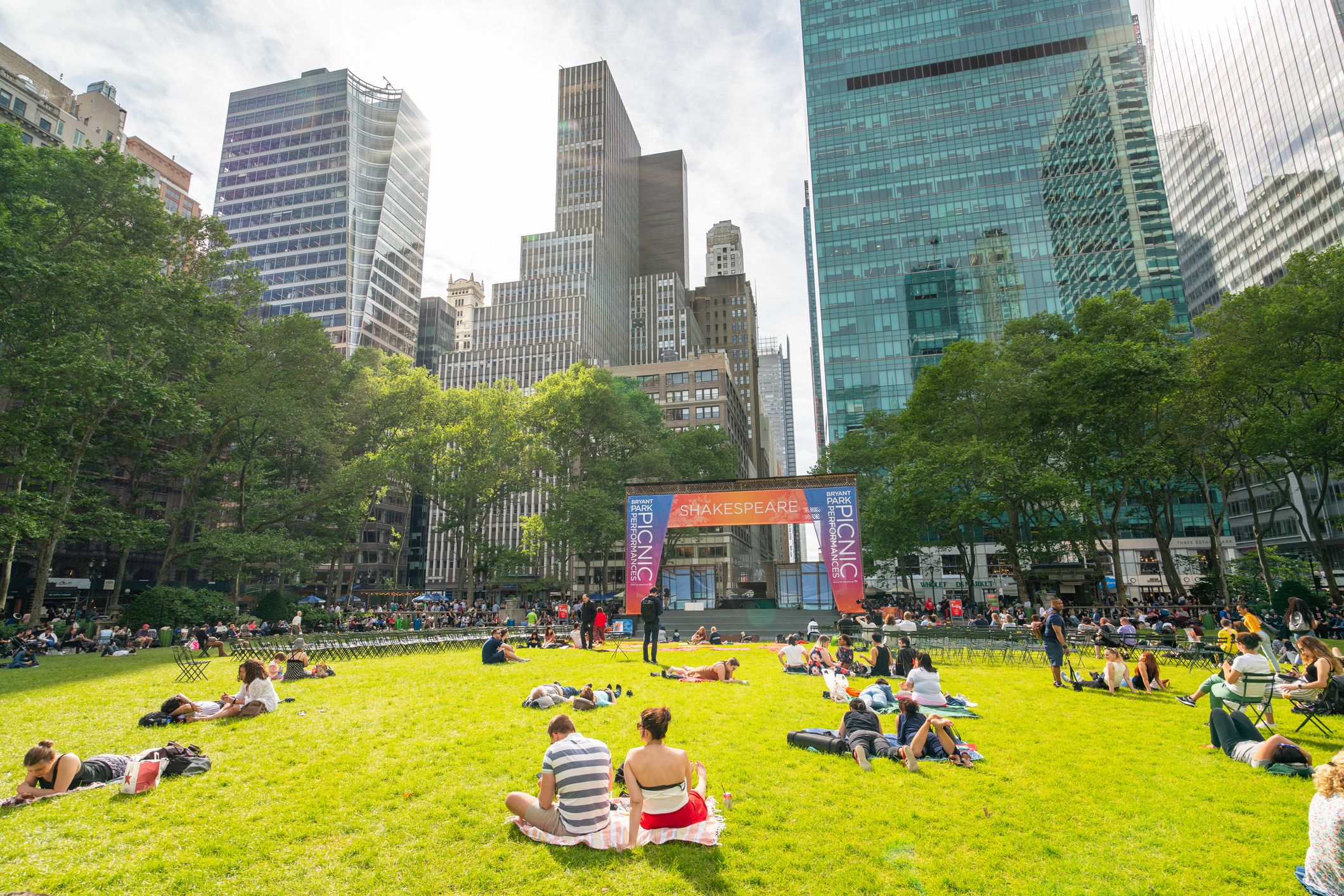 People on the lawn of Bryant Park, Manhattan, surrounded by skyscrapers on a sunny day during summer