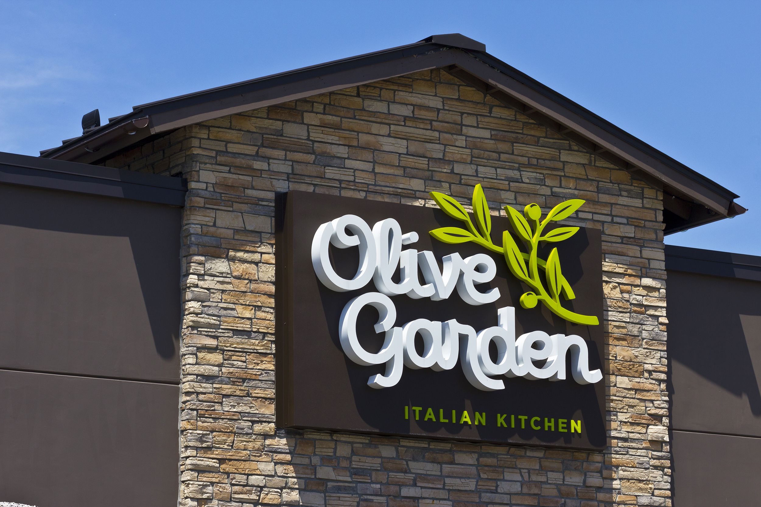 Closeup of sign on exterior of Olive Garden Italian restaurant in Indianapolis, Indiana with a blue sky in the background