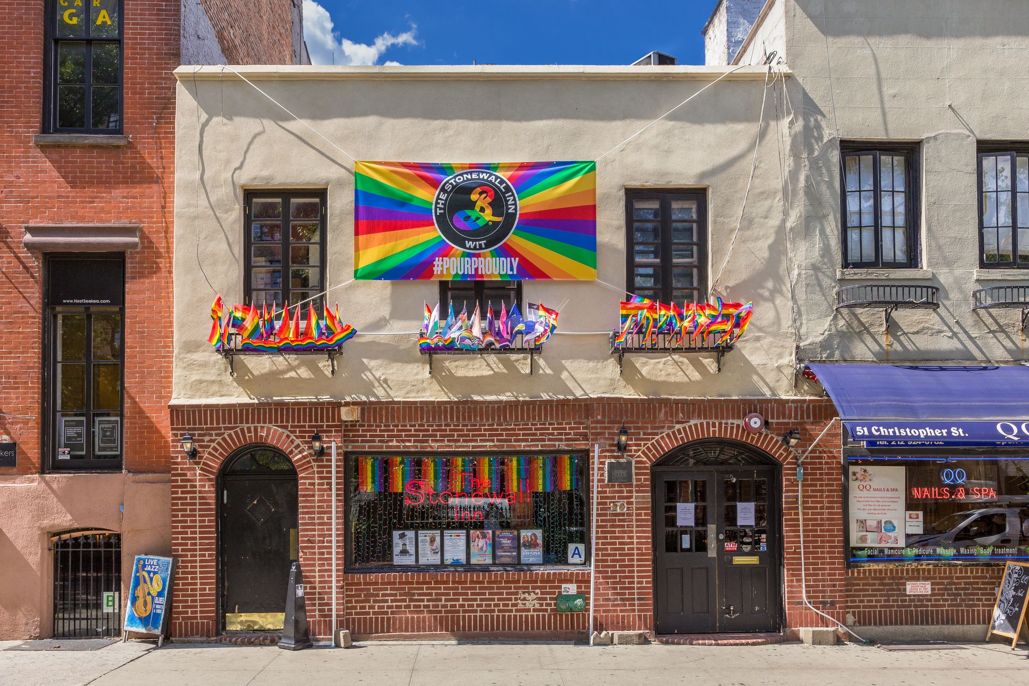 Front exterior of the Stonewall Inn Bar in the West Village, Lower Manhattan, several gay pride flags decorate the building, on a sunny day