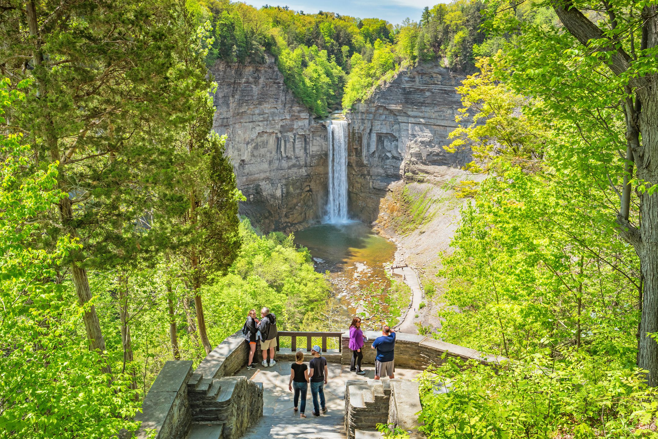 Taughannock Falls near Ithaca, New York, people in the foreground and waterfall in the background, surrounded by trees with light green leaves, on a sunny day