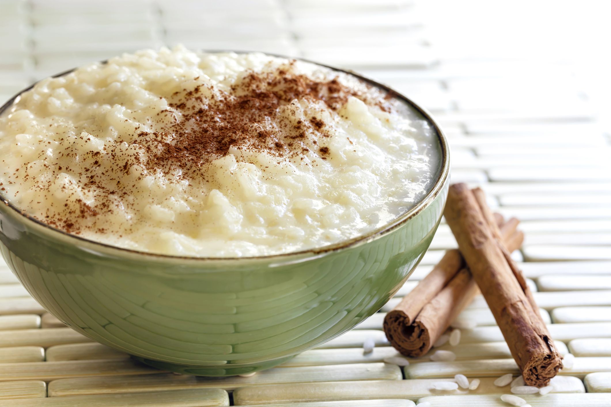 The best pressure cooker (instant pot) rice pudding in a green ceramic bowl with two cinnamon sticks on a bamboo table