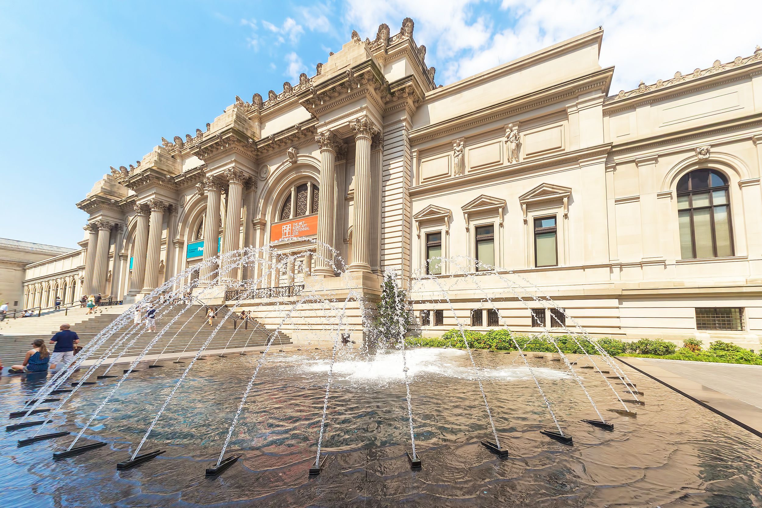 The Metropolitan Museum of Art, Manhattan, fountain in the foreground with front of the building in the background, with a blue sky with white clouds on a sunny day