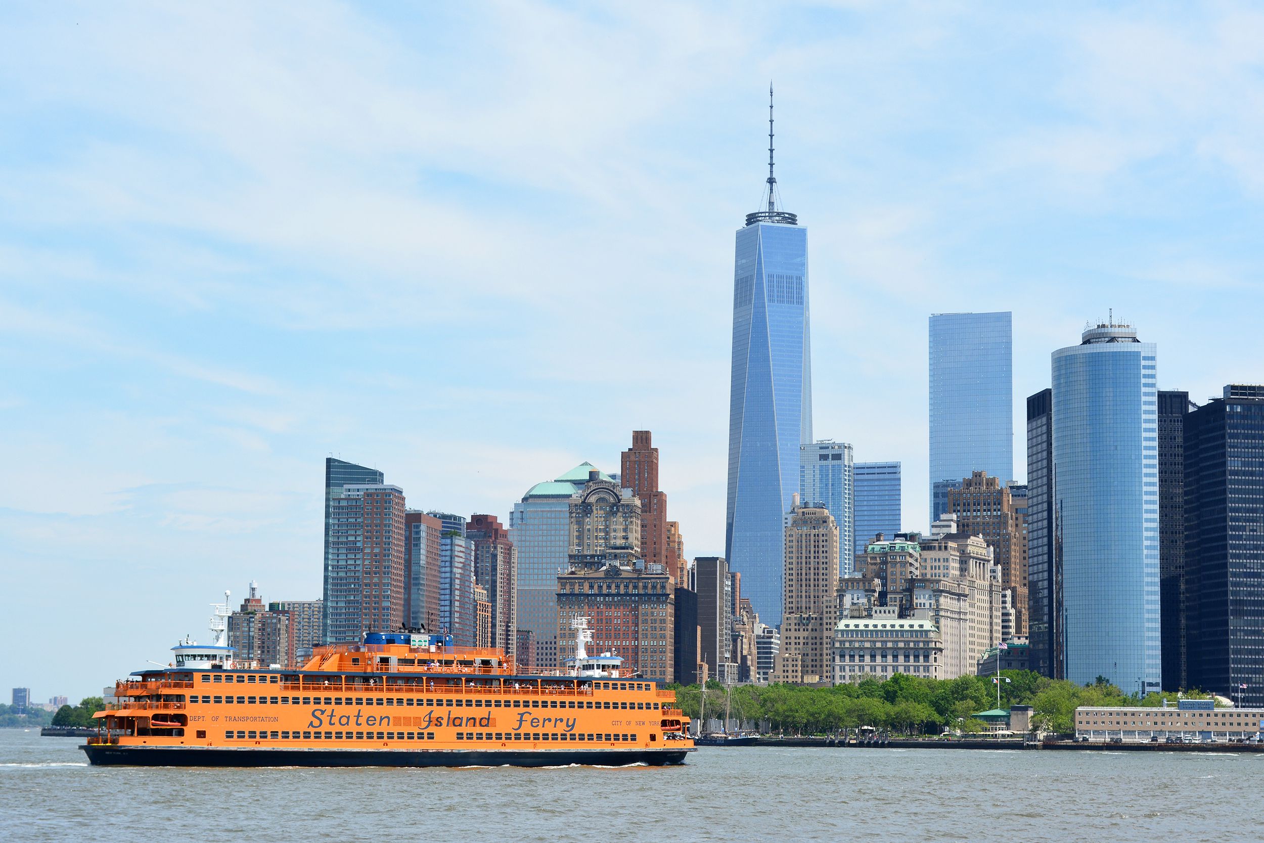 The Staten Island Ferry pulling into New York Harbor with the lower Manhattan skyline in the background on a sunny day
