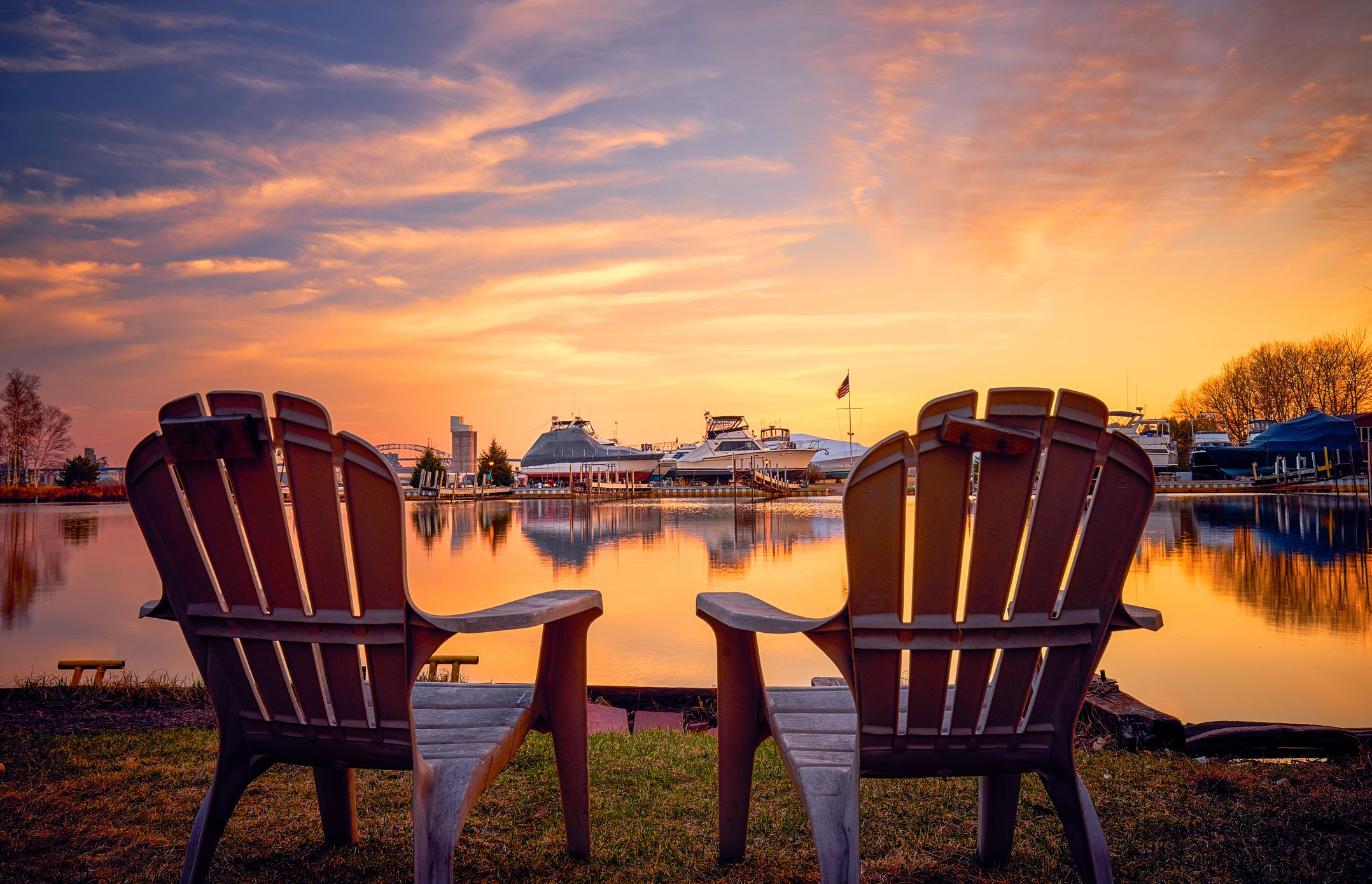 Two adirondack chairs in the foreground on the bay side of Park Point, Duluth, Minnesota during sunset