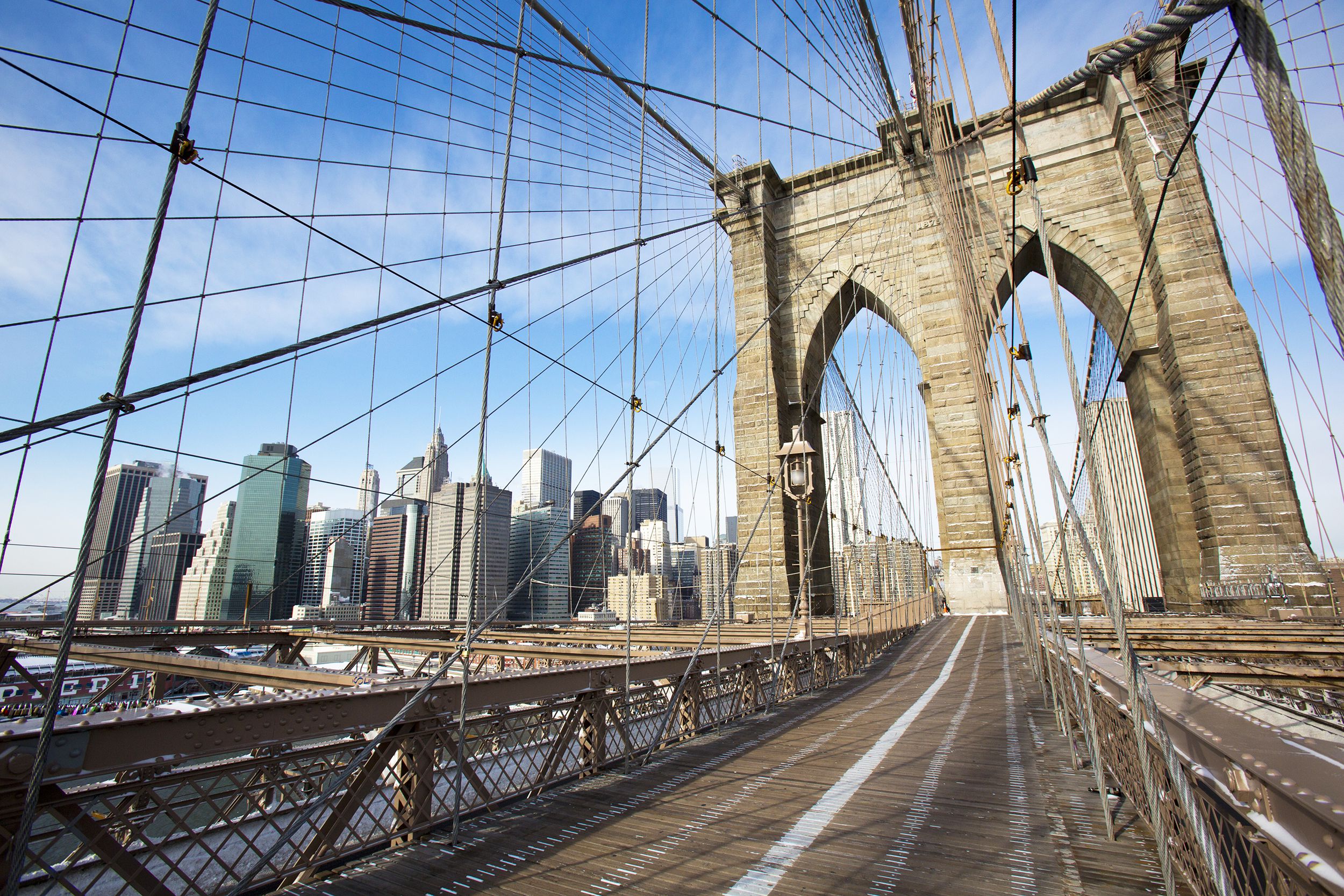 Walkway in the Brooklyn Bridge, New York City, dramatic view with Manhattan Financial District in the background, with a clear blue sky on a sunny day