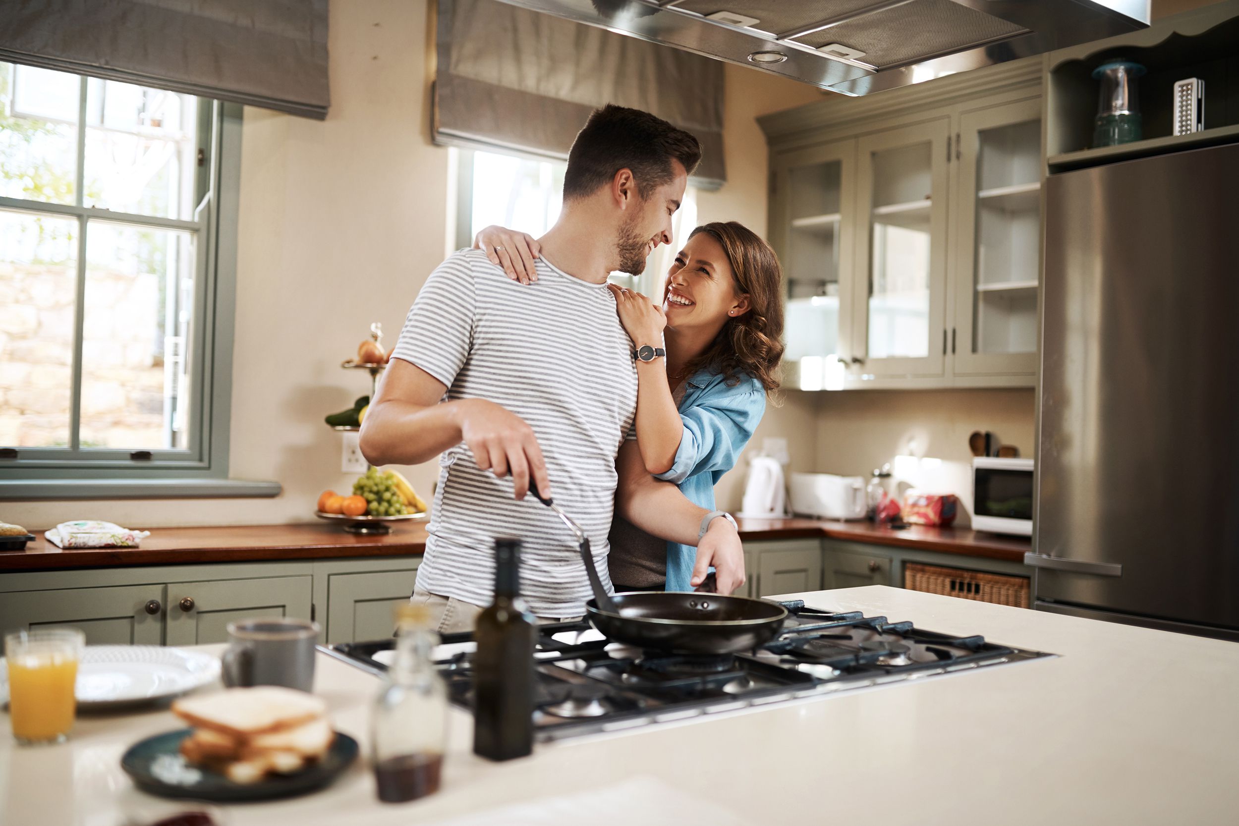 young woman embracing her partner while he cooks breakfast
