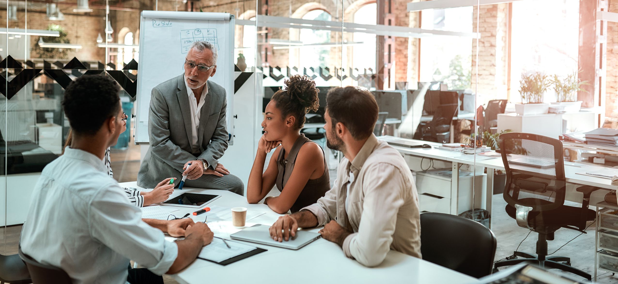 Working process. Mature businessman talking about something with his young colleagues while sitting together at the office table in the modern office. Teamwork. Business concept