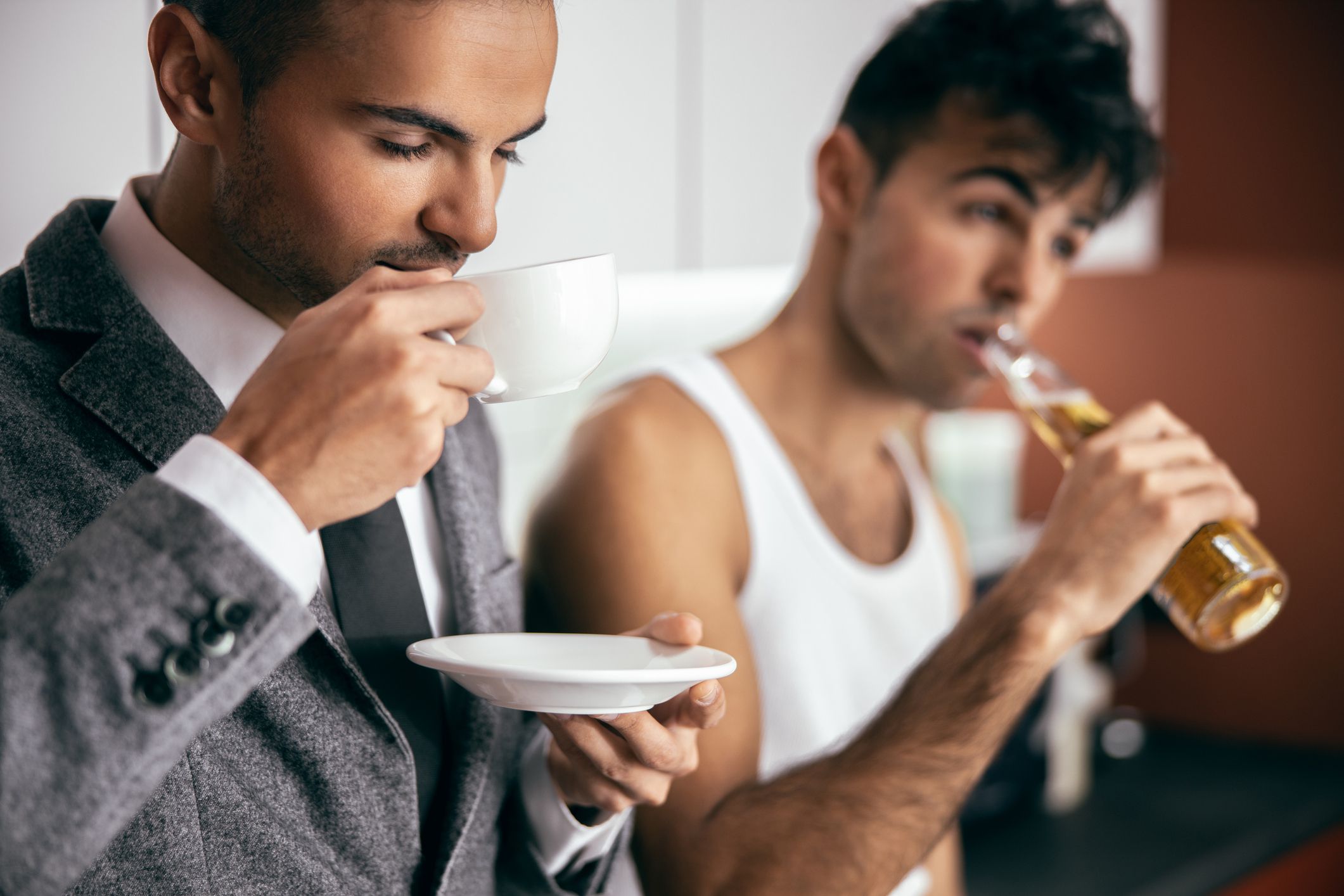 Two brothers holding hot drink and beer while standing together at home stock photo