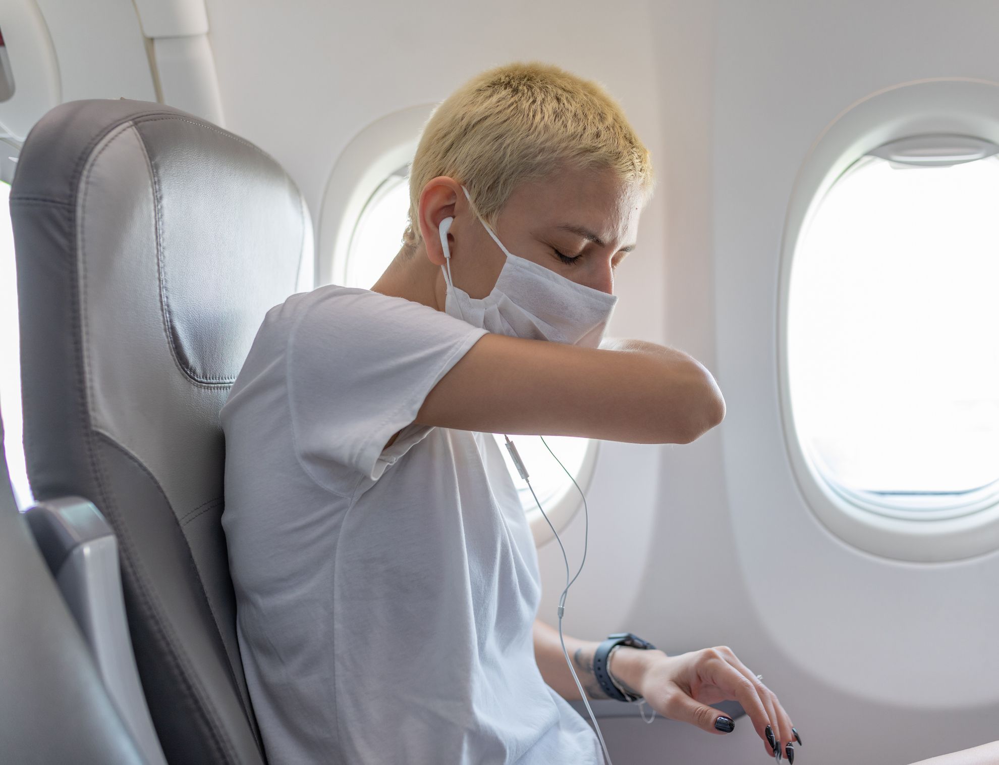 Portrait of woman in face mask flying on a plane and sneezing