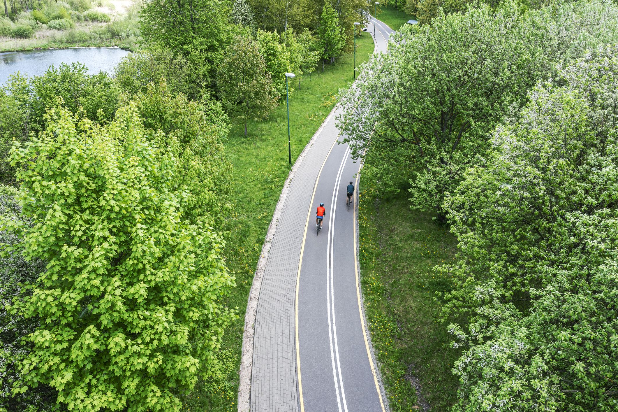 two cyclists ride bikes on bicycle path in city park at spring day. aerial photography with drone.