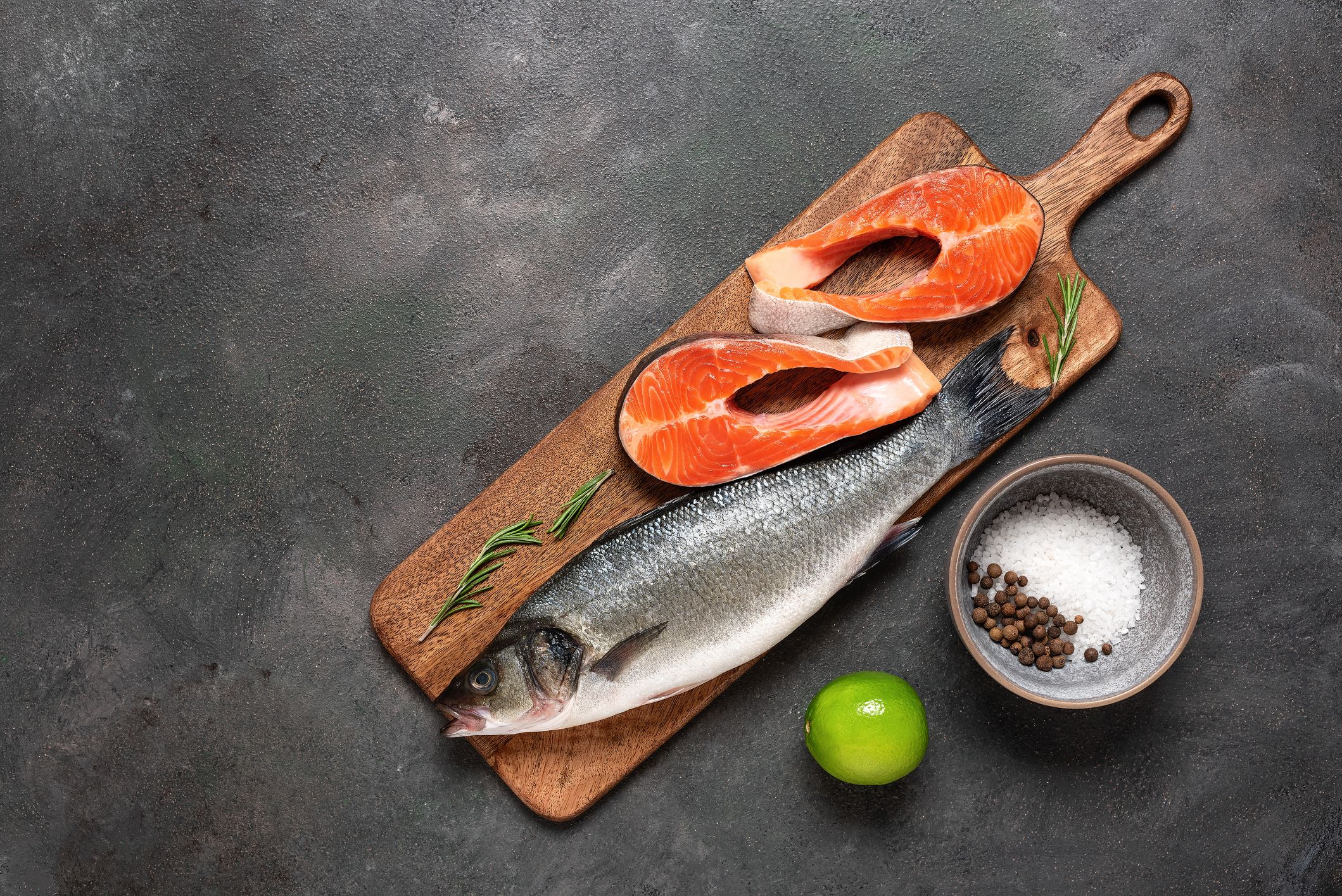Raw fresh fish sea bass and trout on a cutting board, dark rustic background. Top view, flat lay