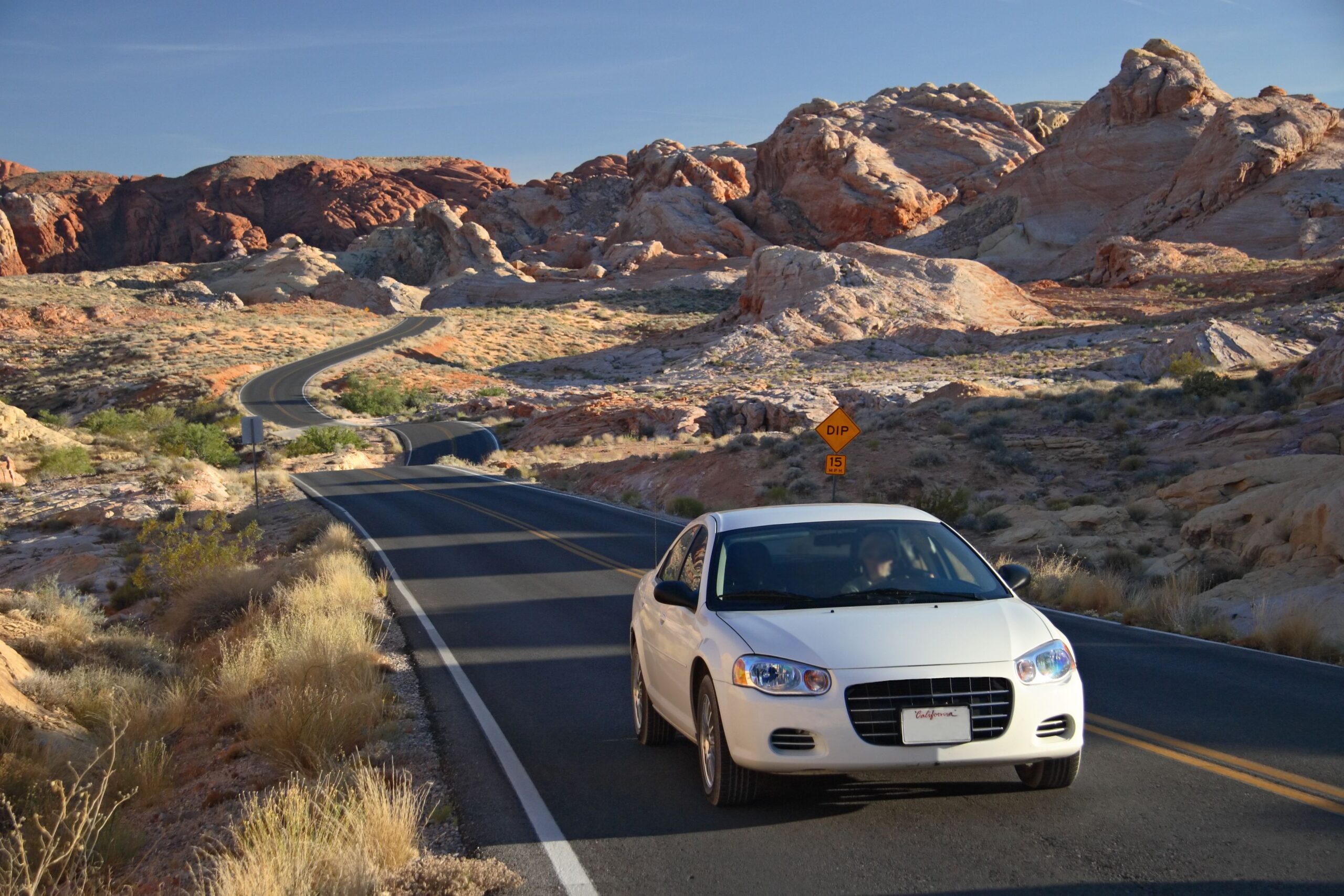 Midclass car on a scenic, winding road leading to Mountains in the Valley of Fire State Park in Nevada near sunset