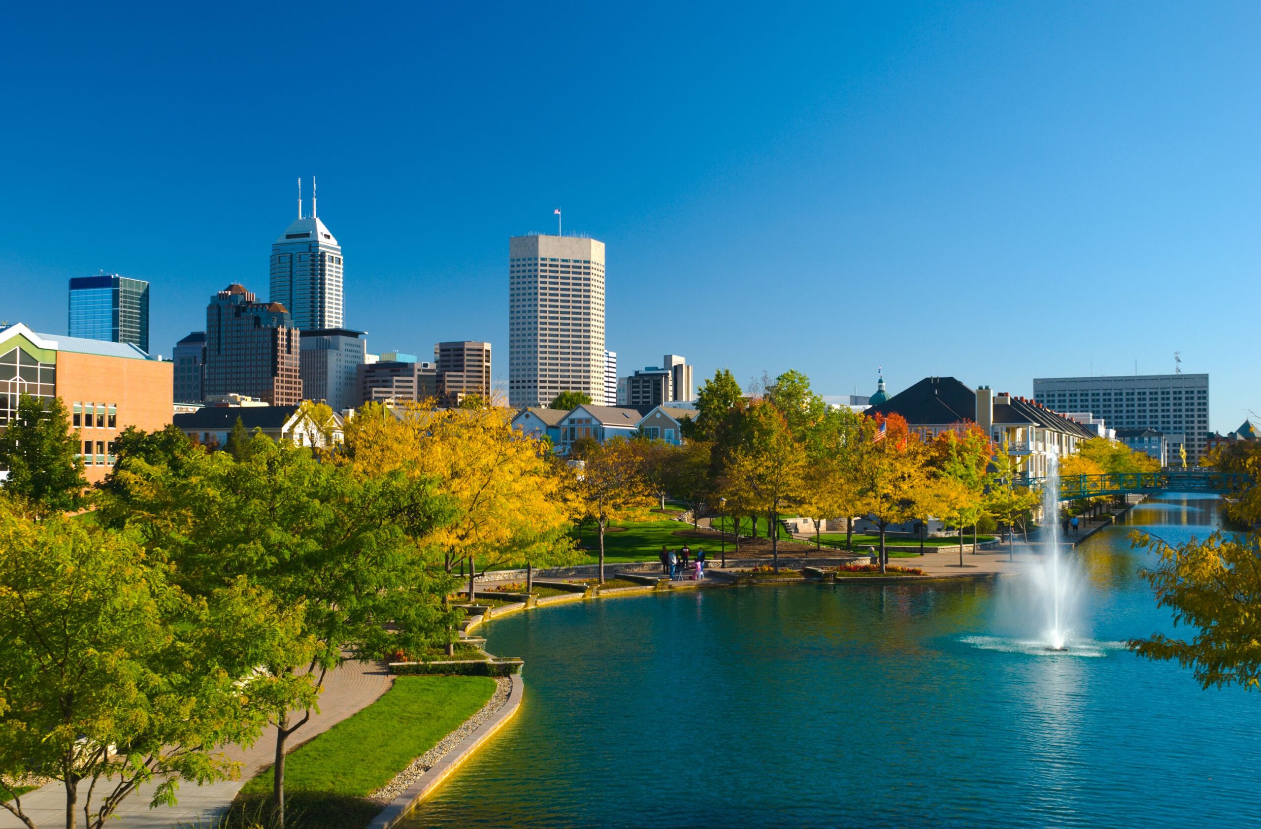 Indianapolis skyline in the distance with houses and the Indiana Central Canal / Canal Walk in the foreground.
