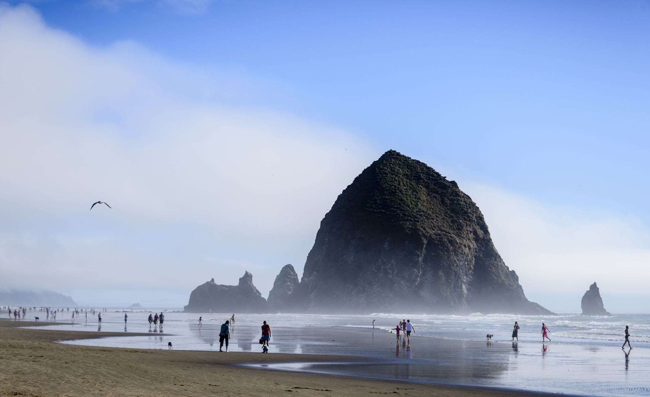 People enjoying a day at Cannon Beach, Oregon. The formation known as Haystack Rock can be seen in the background.
