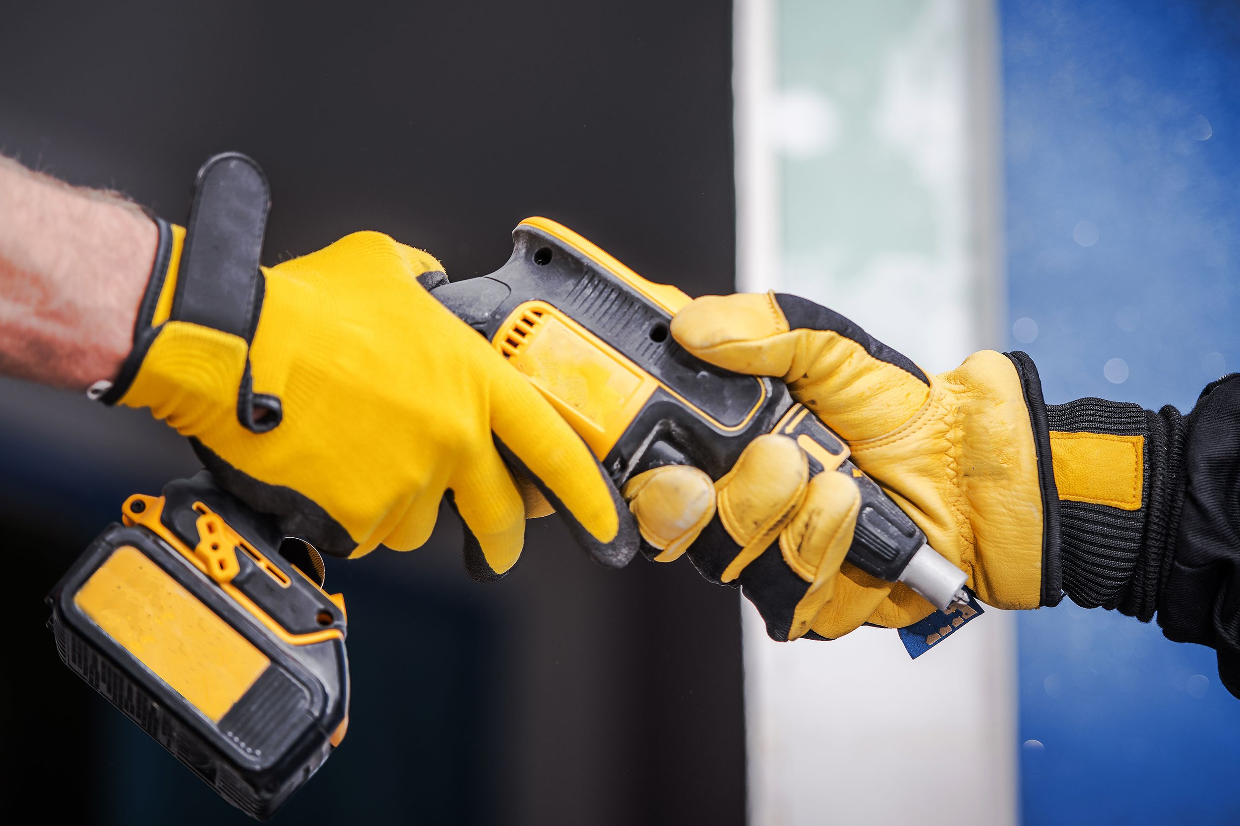 gloved hand giving power tool to another gloved hand