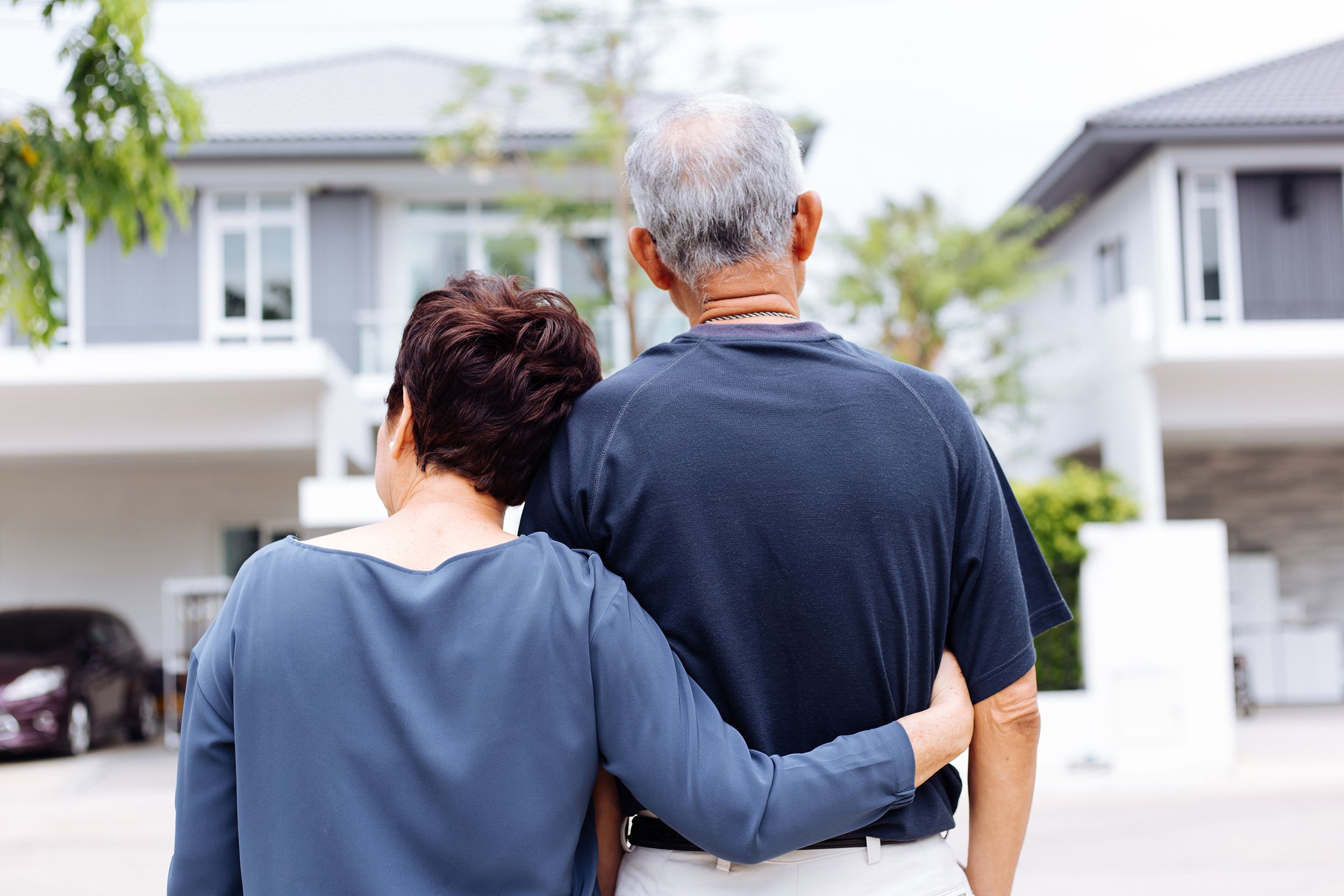 happy senior couple from behind looking at front of house and car