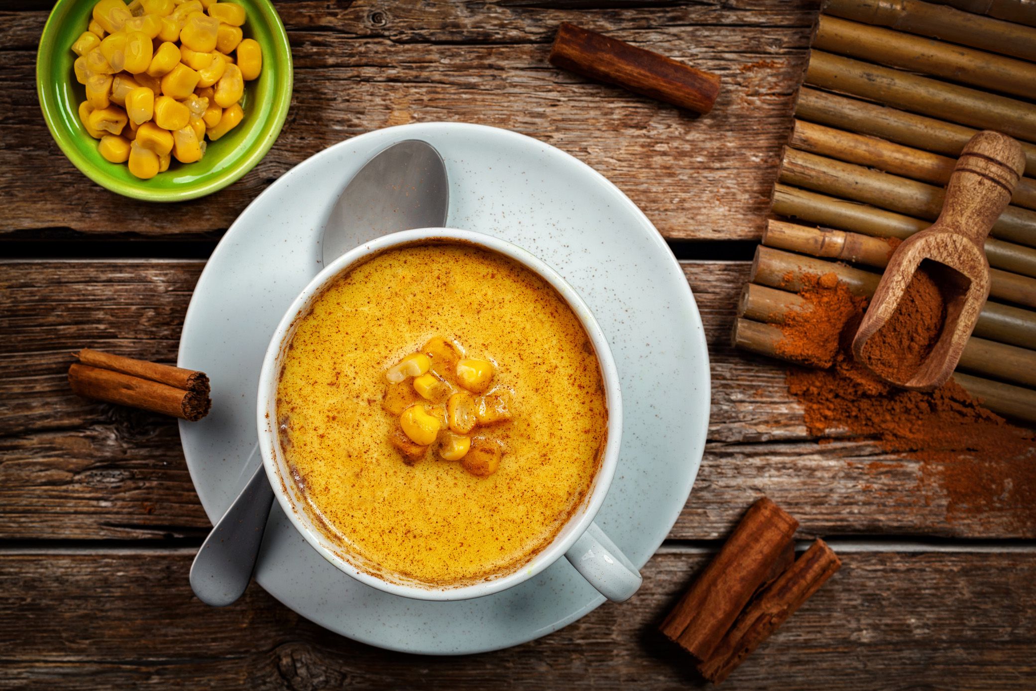 Atole with cinnamon and corn in a white cup, with cinnamon sticks and ground cinnamon on a rustic wood table