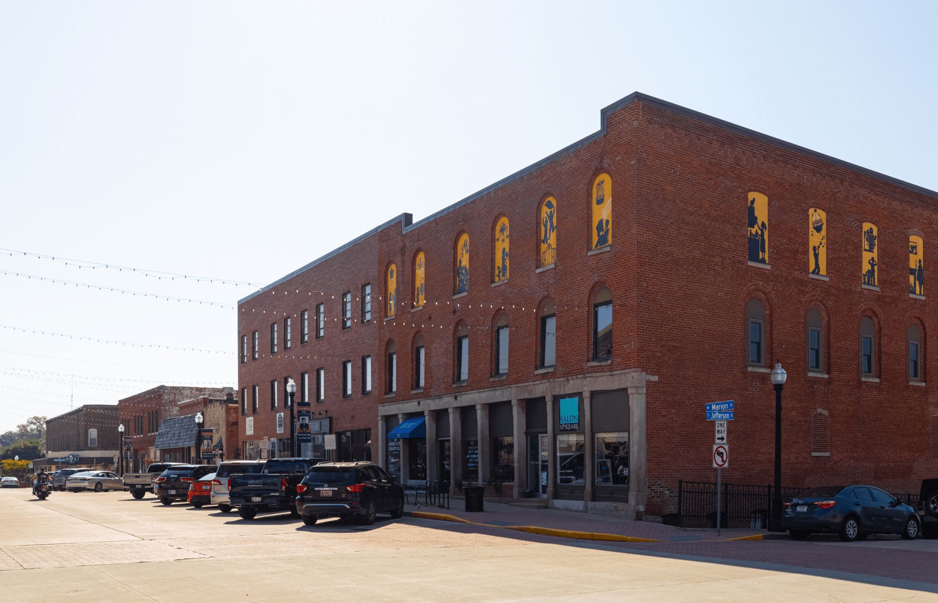Business district on Marion Street, Danville, Indiana, large brick building with a row of storefronts to the left with parking, road in the foreground, against a light blue sky in summer