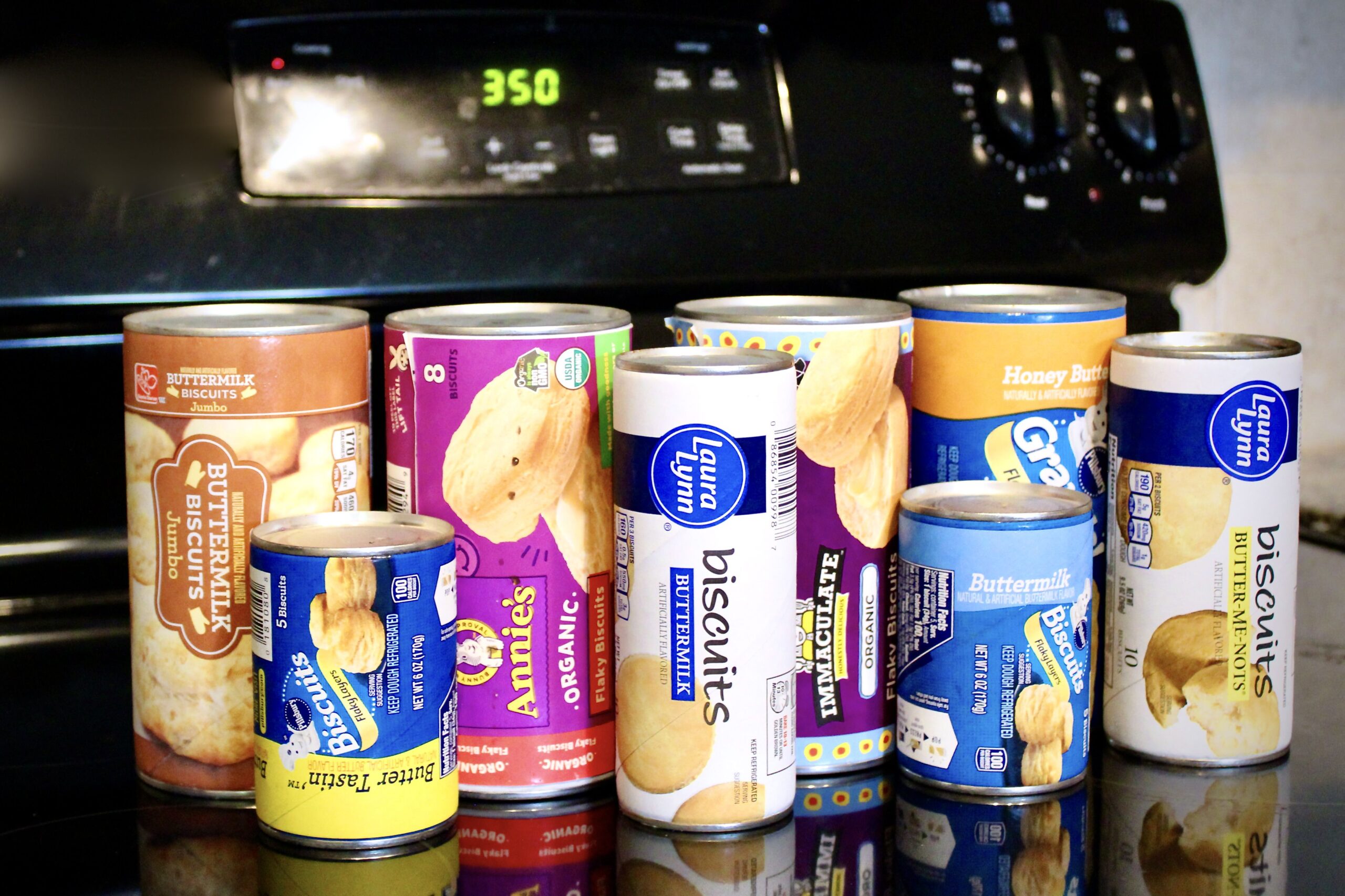 Various brands of canned biscuits lined up on an oven