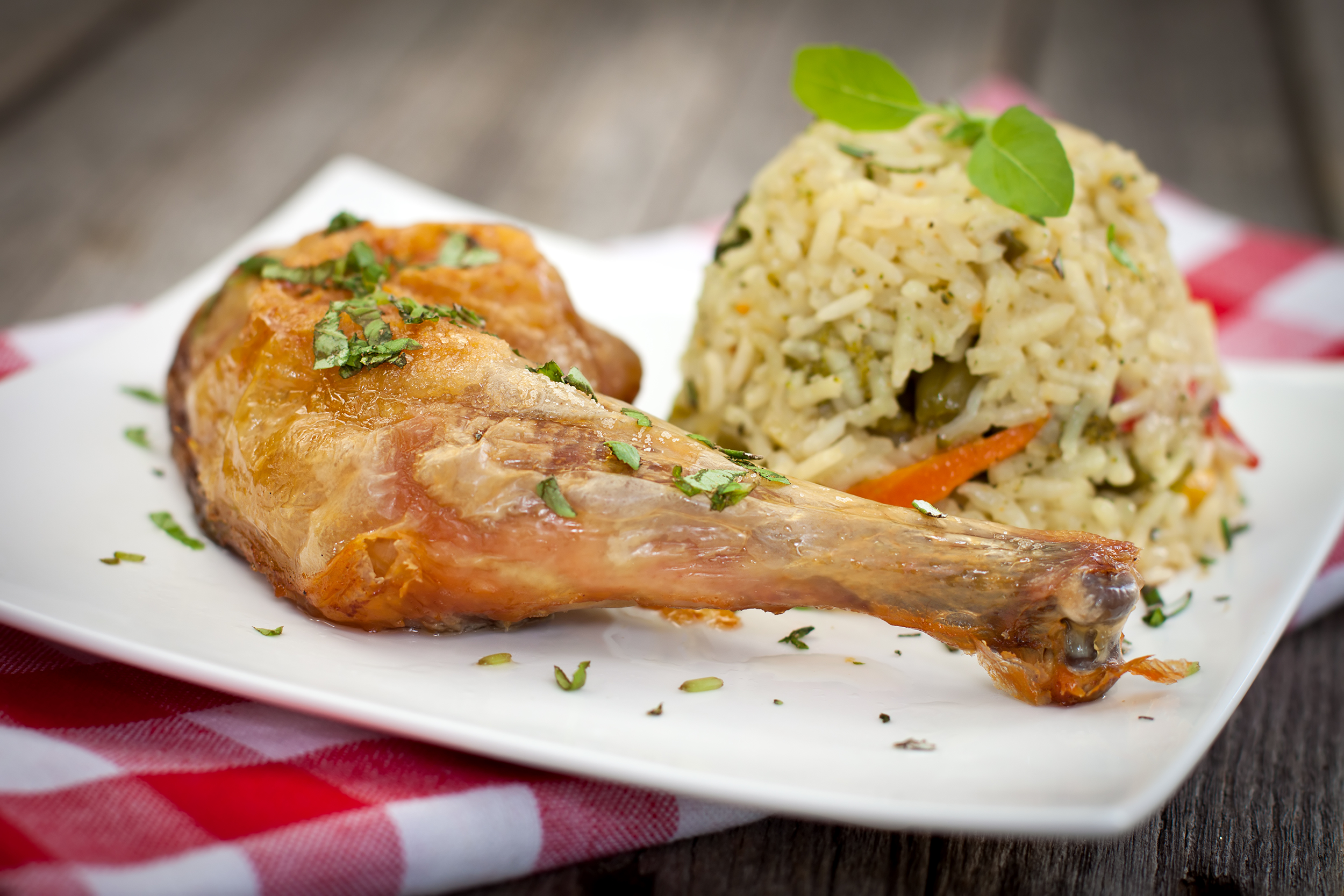 Chicken with veggie rice pilaf, selective focus, on a square white porcelain plate, on a red and white checkered napkin, on a wooden table, blurred background
