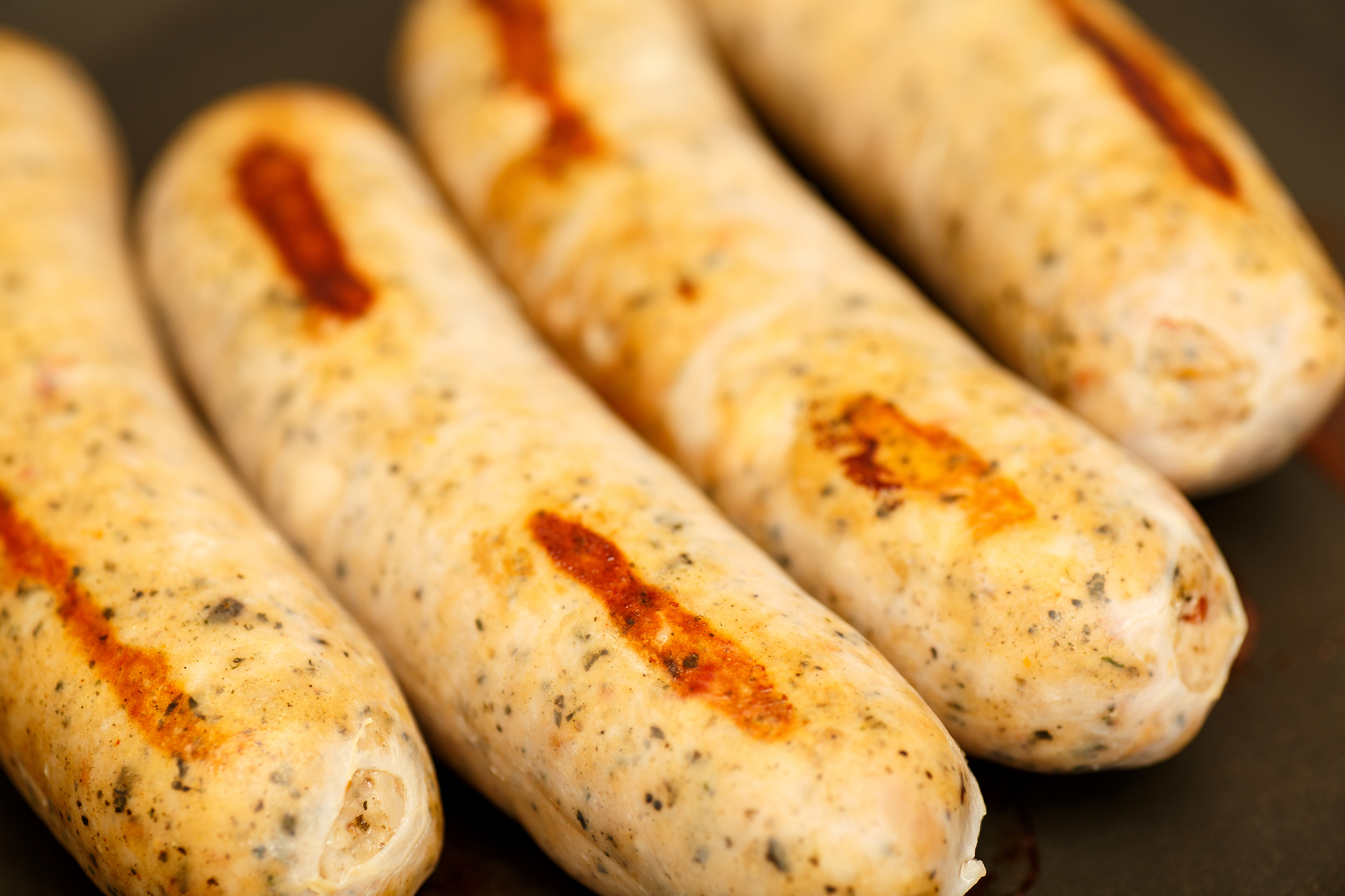 Closeup of four chicken & apple sausages on a black plate, blurred at the top