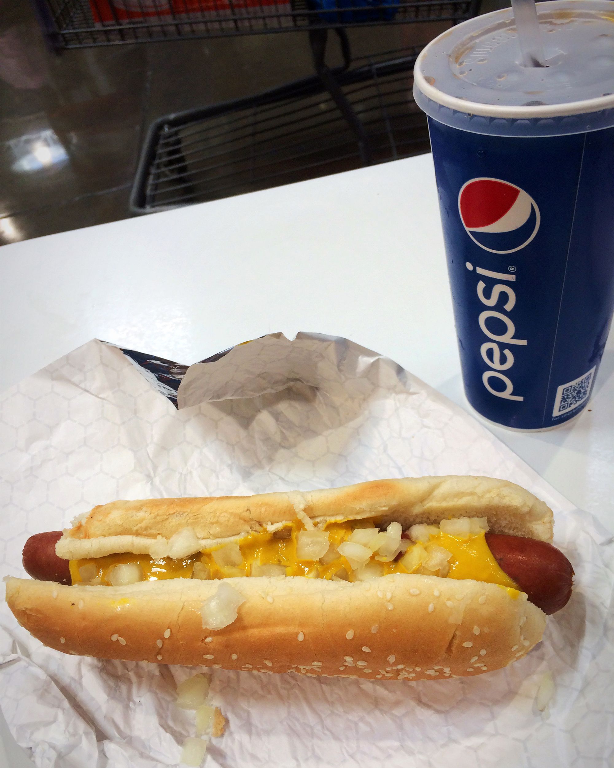 Costco lunch $1.50, hot dog and soda, on a white table at Costco, with the floor and seating in the top