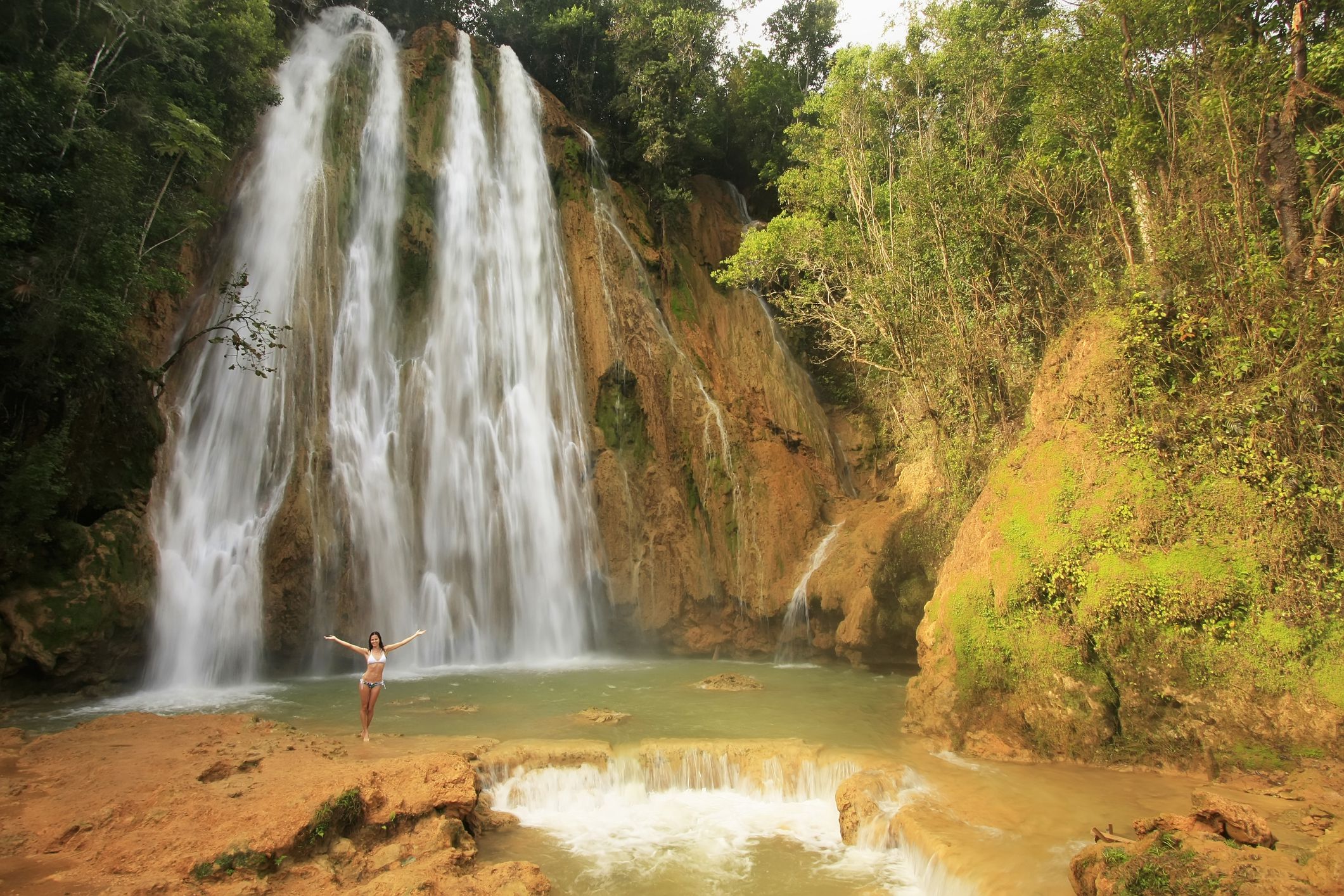 El Limon Waterfall, Dominican Republic with swimming hole, a woman is standing near swimming hole with arms open