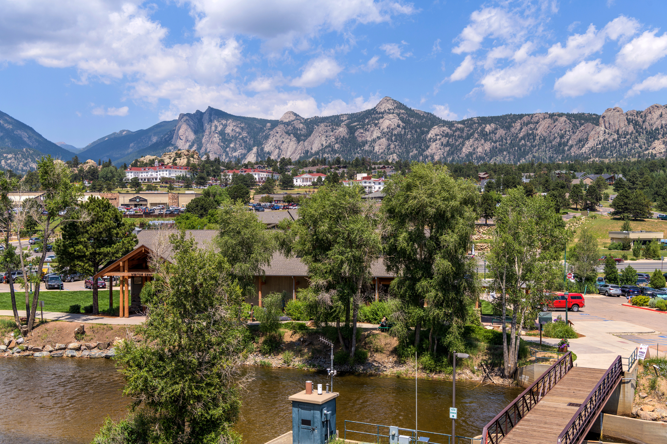 Estes Park, Colorado, during summer, Big Thompson River in the foreground with trees and shopping behind, Rocky Mountains against a blue sky with white clouds in the background