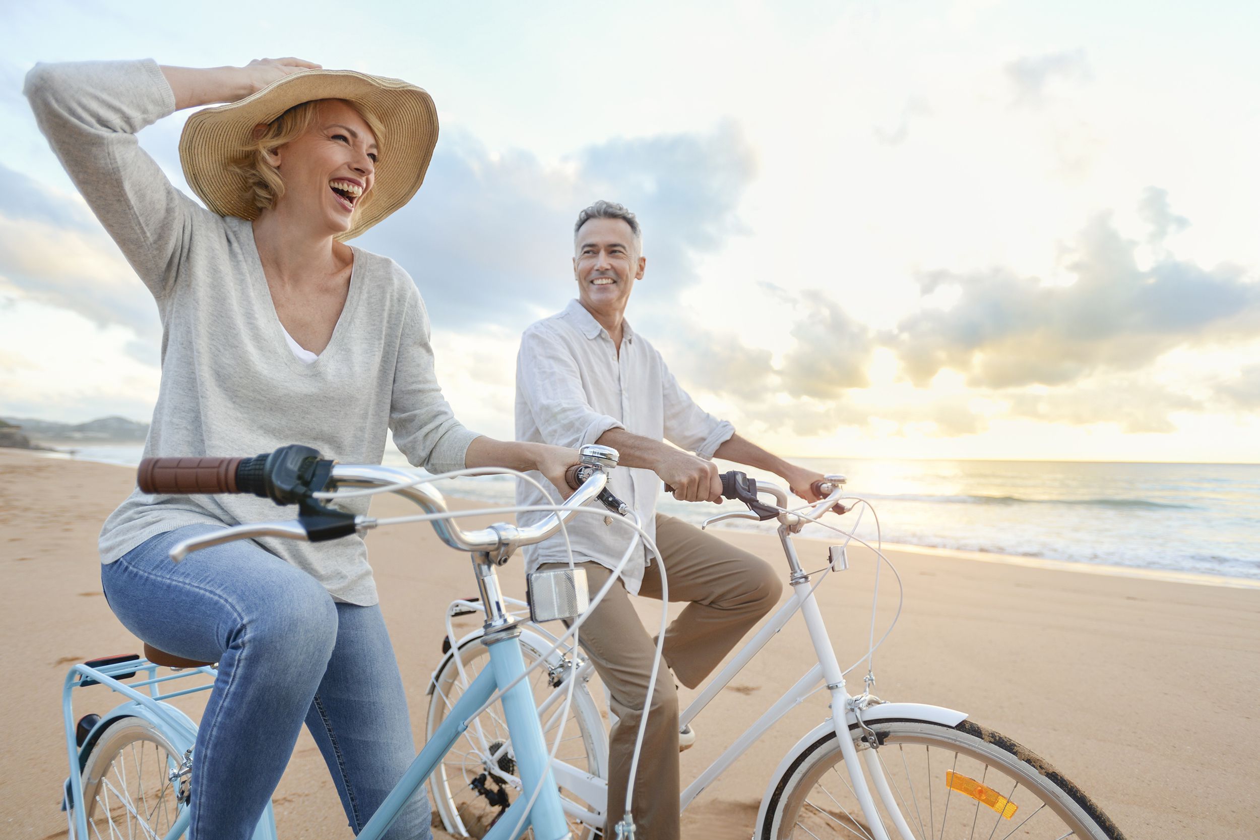 Happy senior couple cycling with bikes on the beach at sunrise