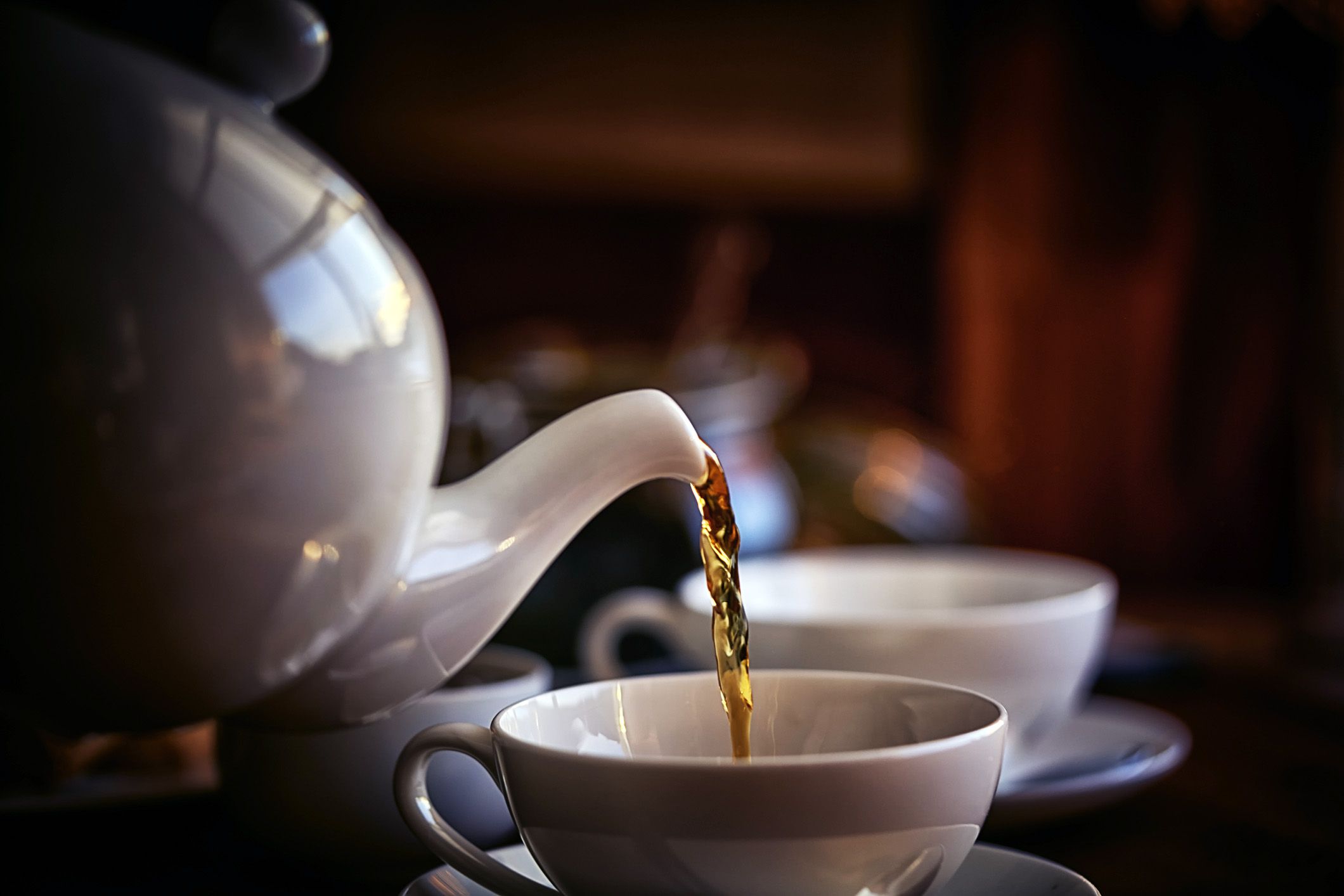 Teapot pouring black tea into tea cup