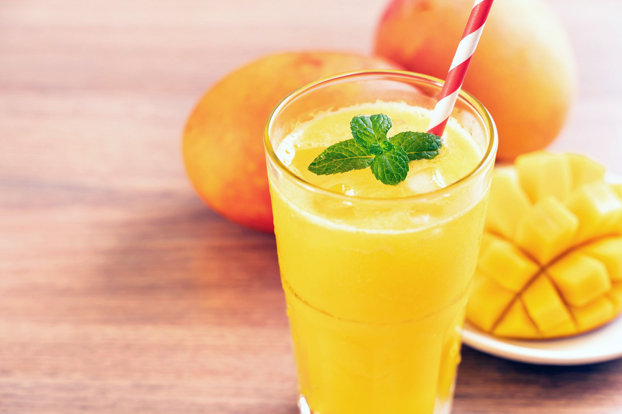Mango smoothie with ice and fresh mint leaves and fresh whole and cut mangoes in the background