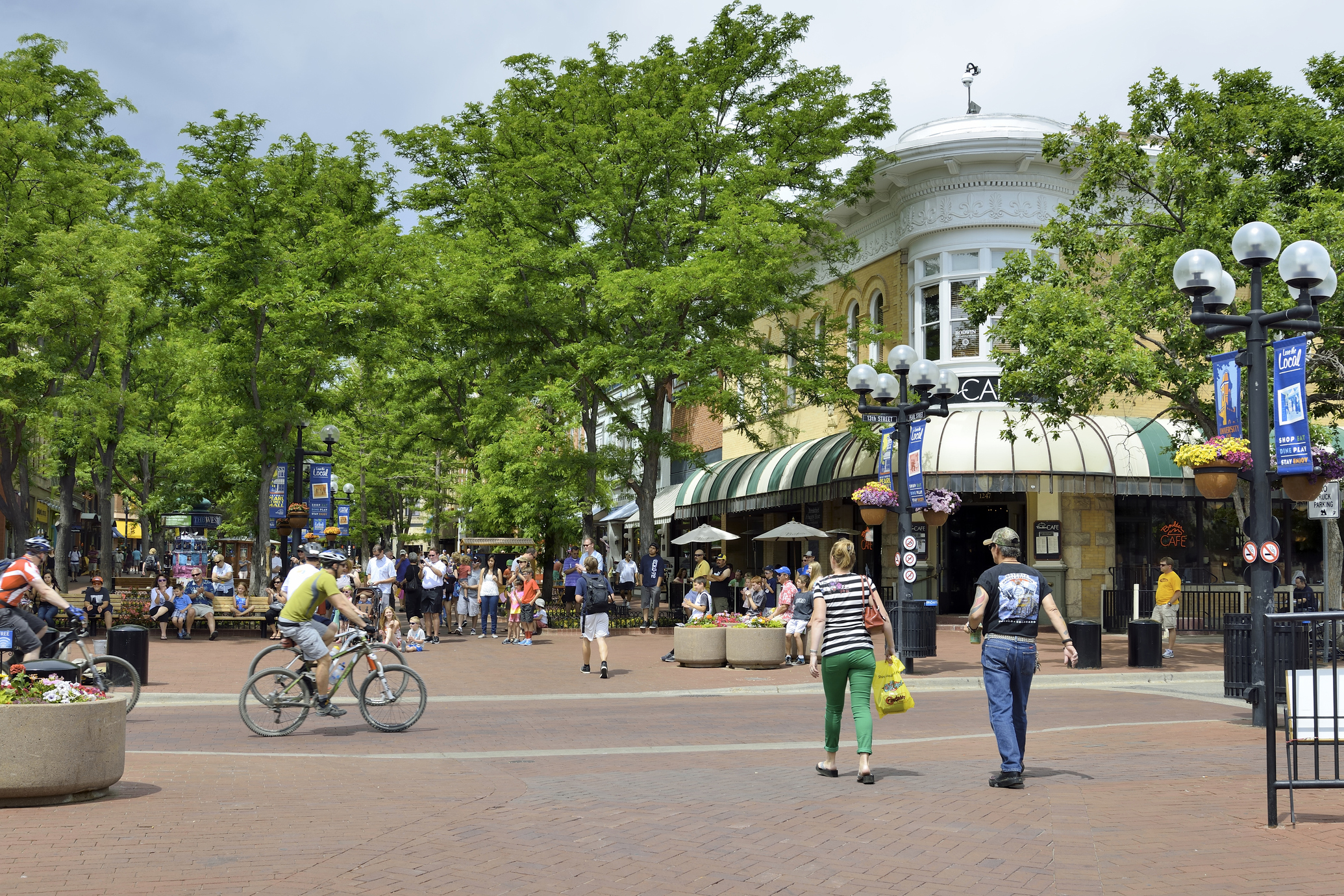 Numerous people along the red brick road of the shopping district of Boulder, Colorado, trees surround the colorful and quaint shops, on a sunny day in summer