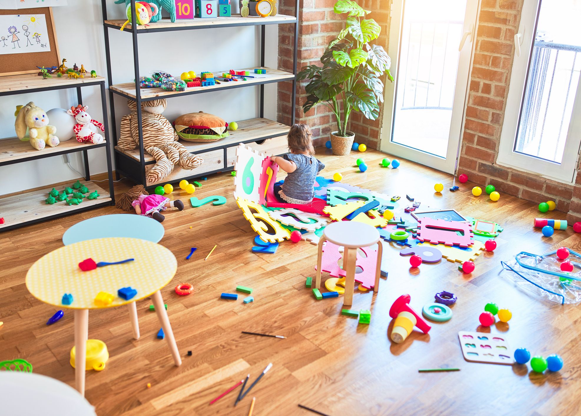 Beautiful toddler sitting on the floor playing with building blocks toy at kindergarten