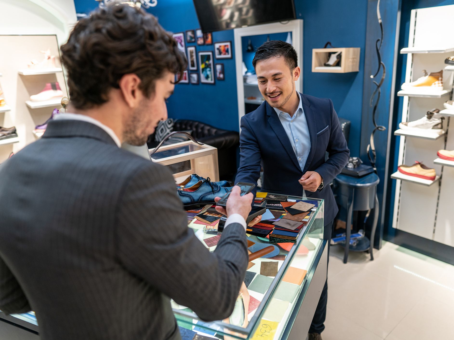 Handsome businessman in suit paying with smart phone, seller using credit card reader at the store