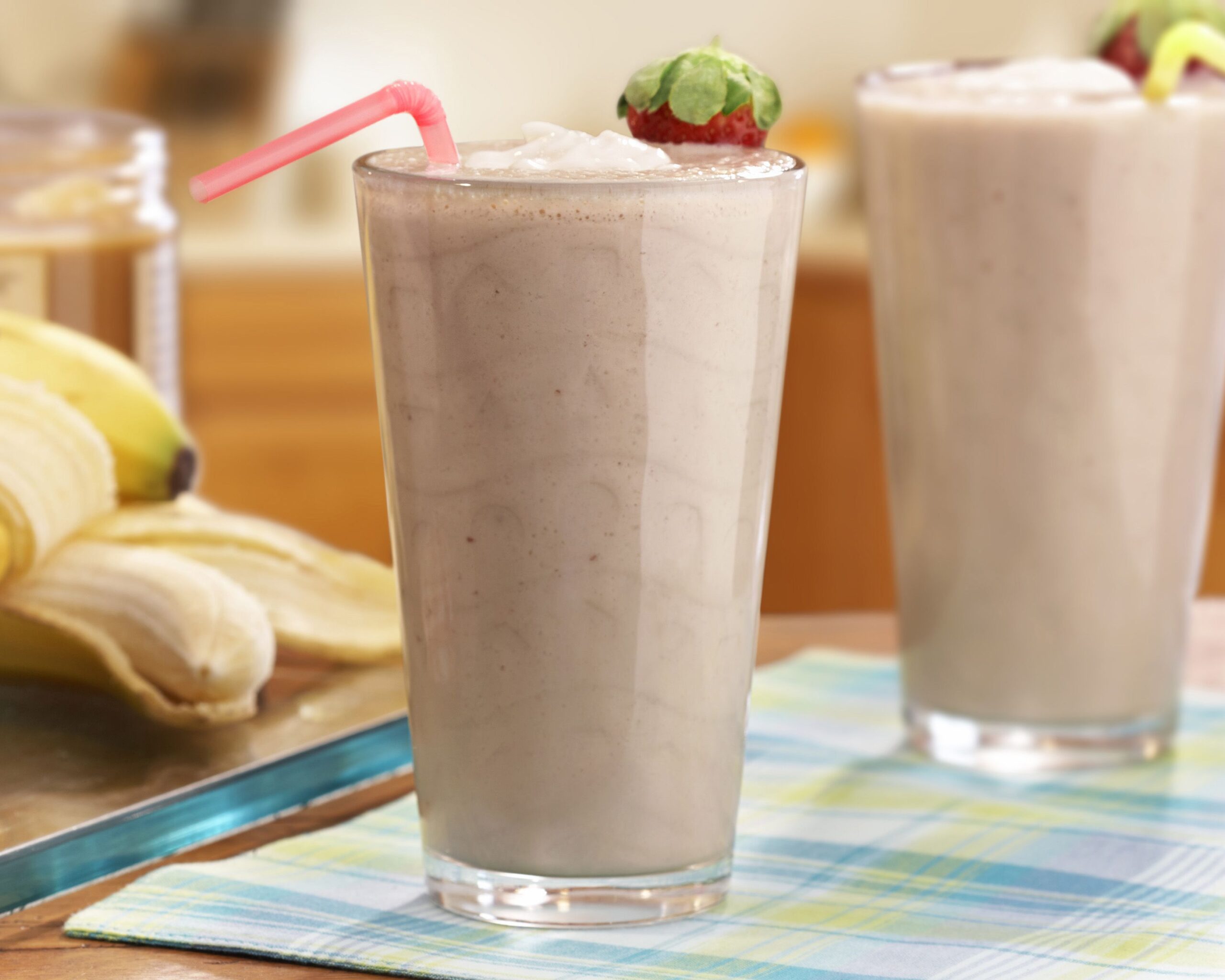 Peanut butter berry smoothies in tall clear glasses with pink and yellow straws and fresh bananas in the background