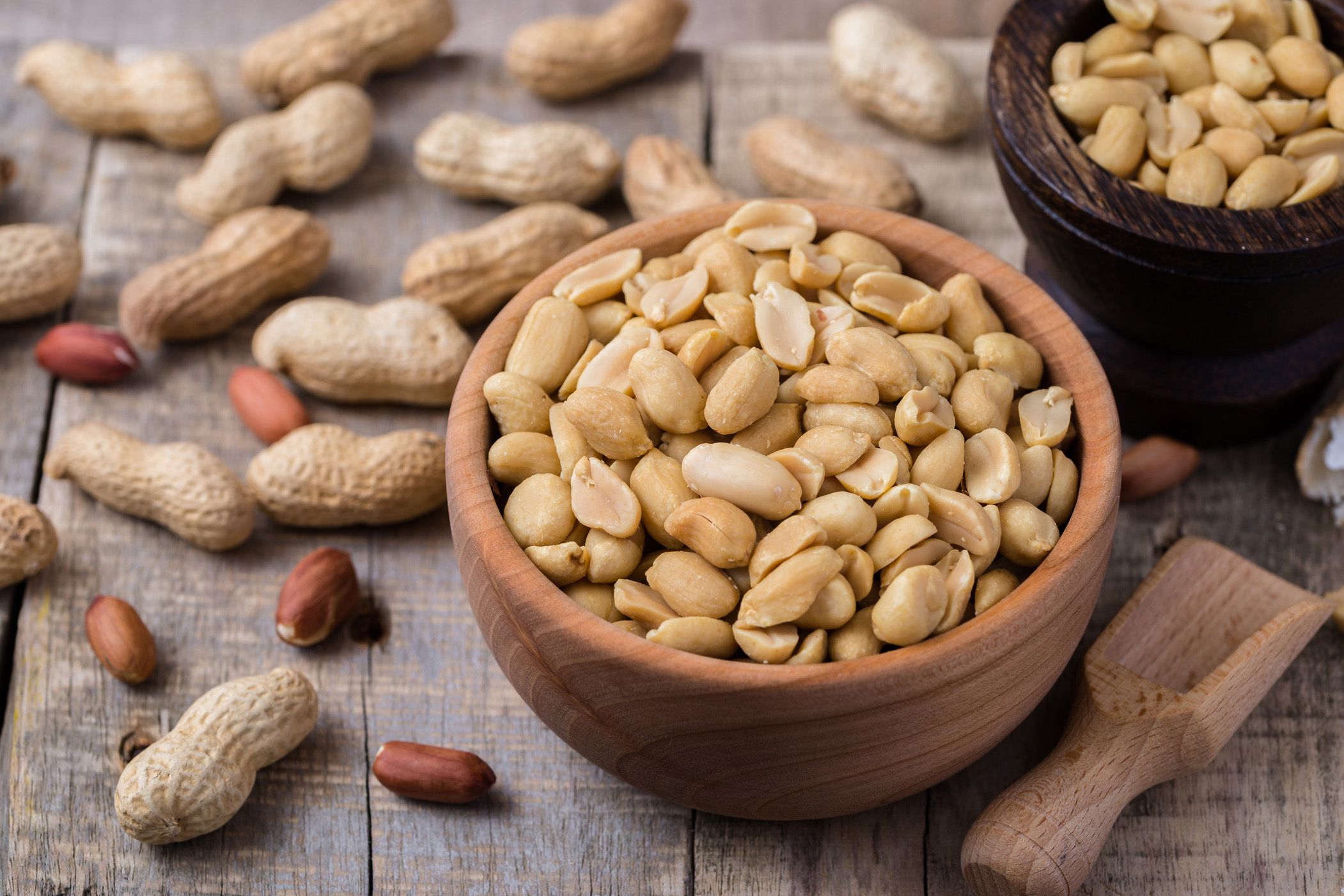 Shelled peanuts in a wood bowl with peanuts in shells on a wood table