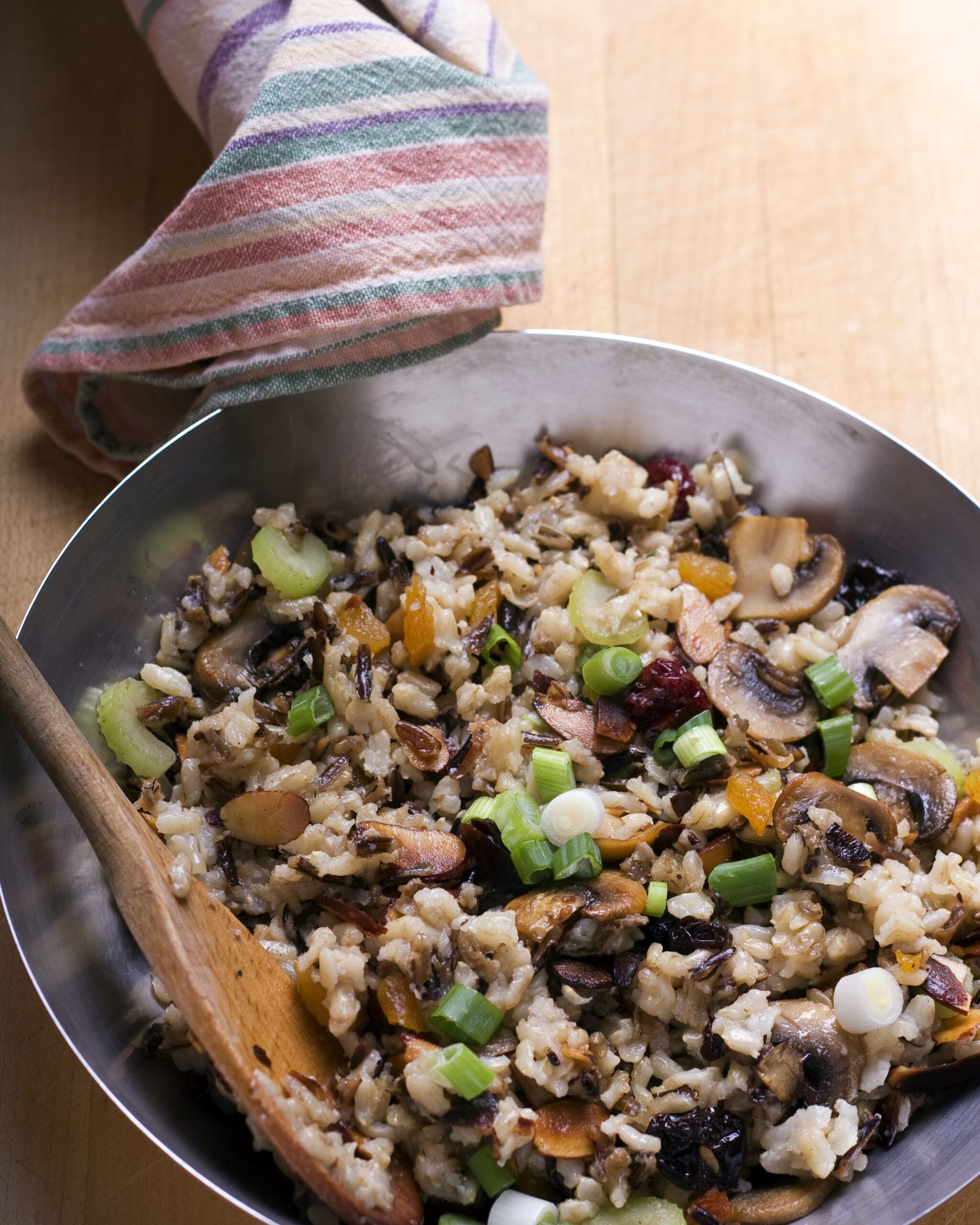 Brown rice pilaf with green onions, dried fruit and nuts in a wok with a wooden spoon