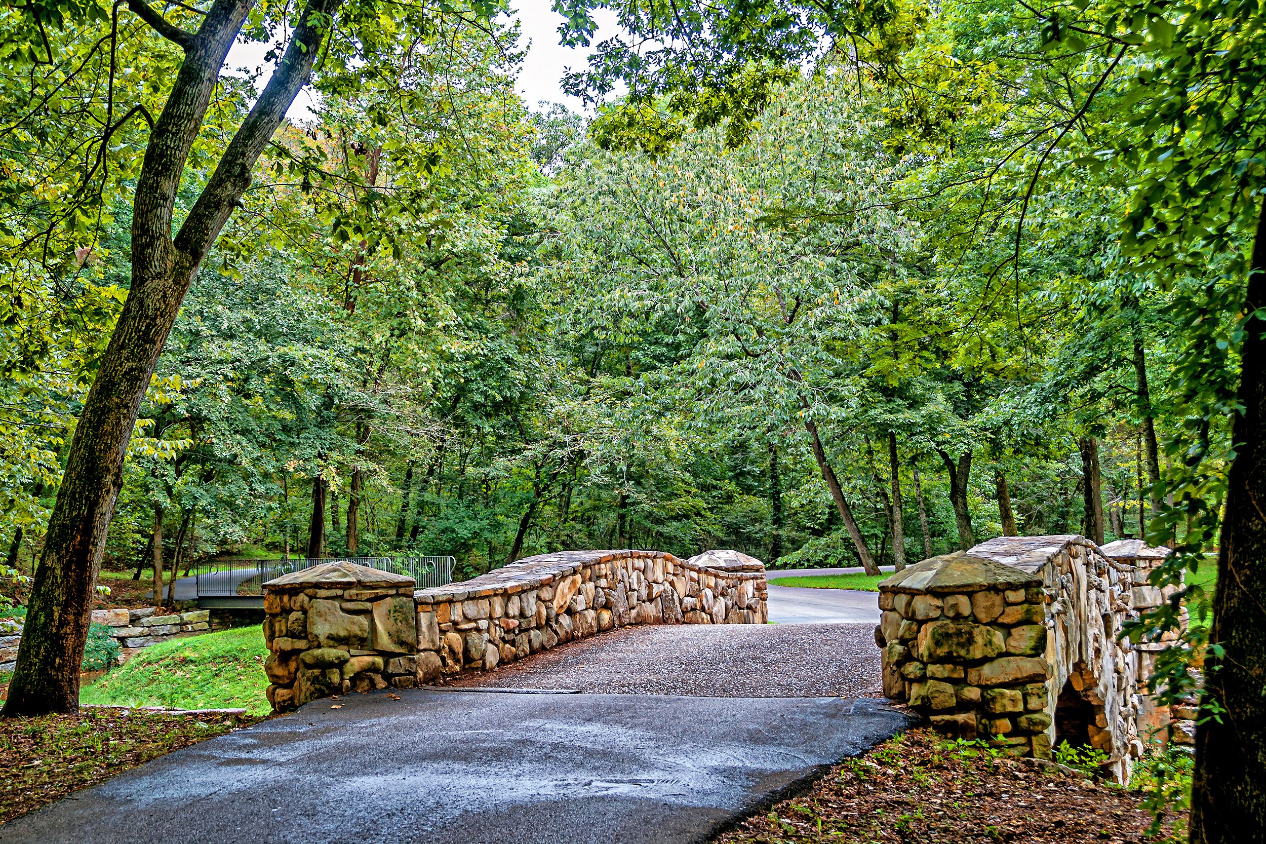 Rustic bridge in Dogwood Canyon Nature Park, Branson, Missouri, road through the bridge in the foreground, numerous trees with green leaves in the background as the road weaves through