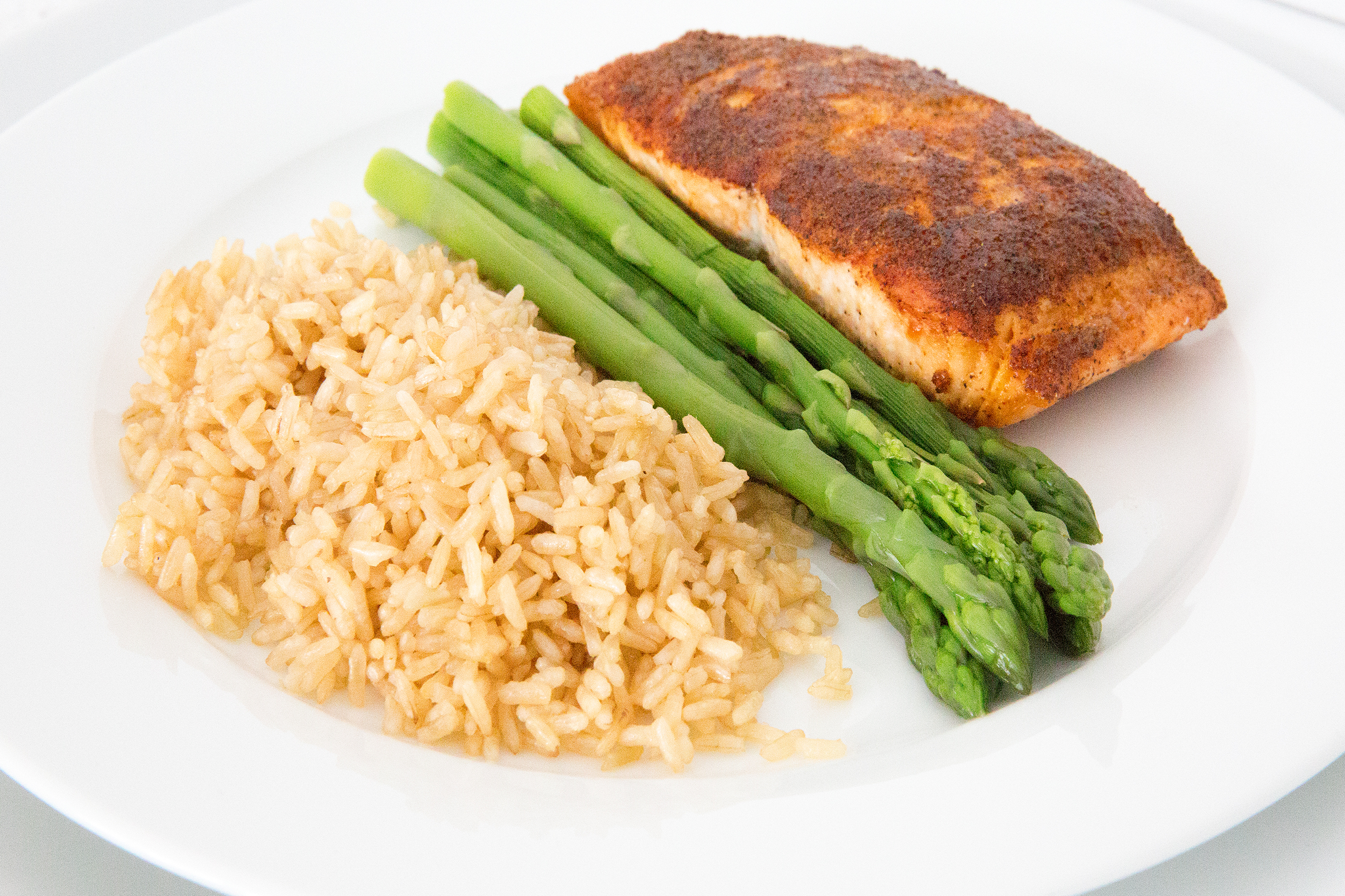 Salmon with brown rice with asparagus in the middle on a white porcelain plate on a white table