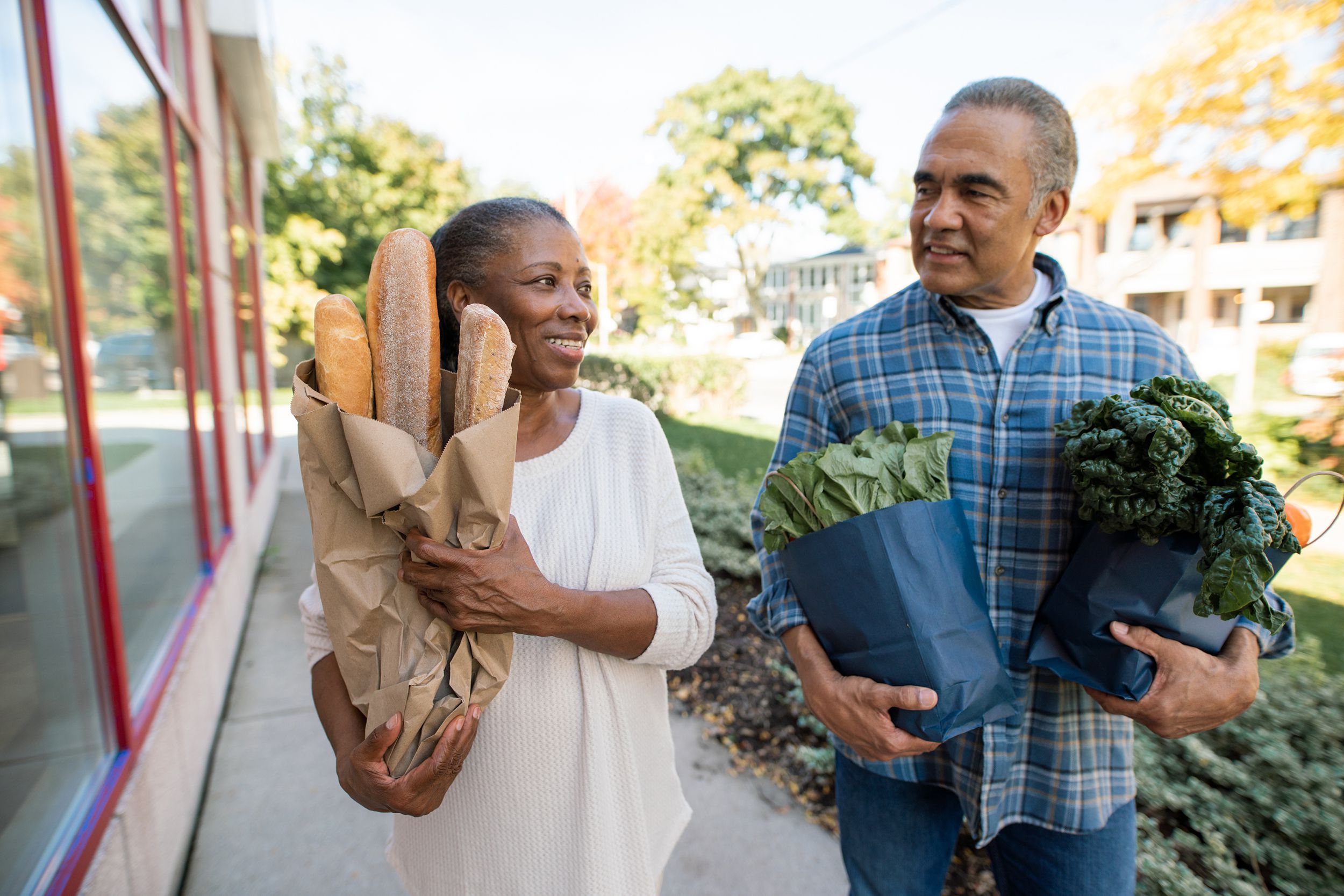 Senior couple holding a few bags of groceries walking outside on a sunny day in autumn