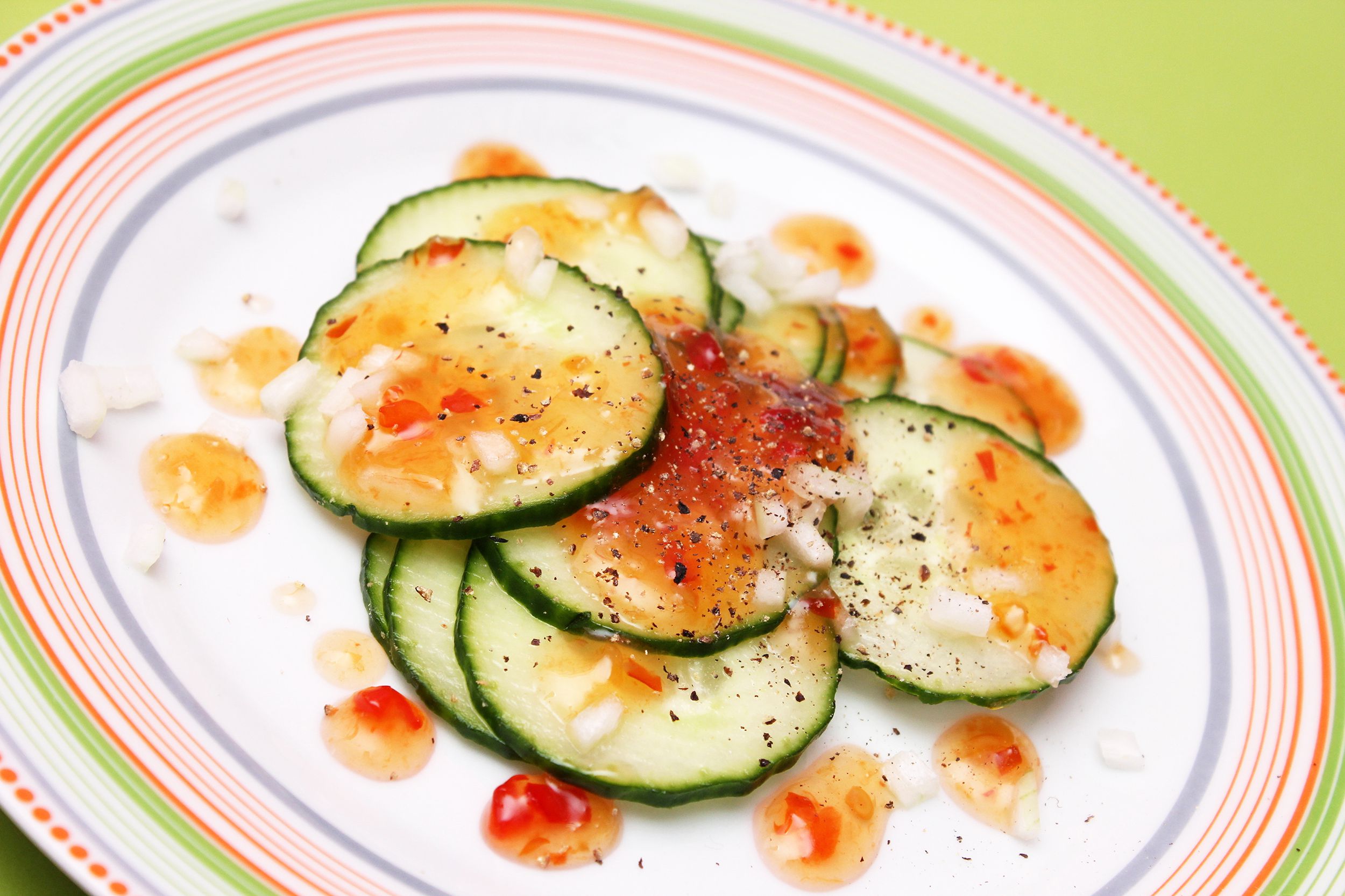 Cucumber slices on a white plate with chili sauce, chopped white onions and ground black pepper