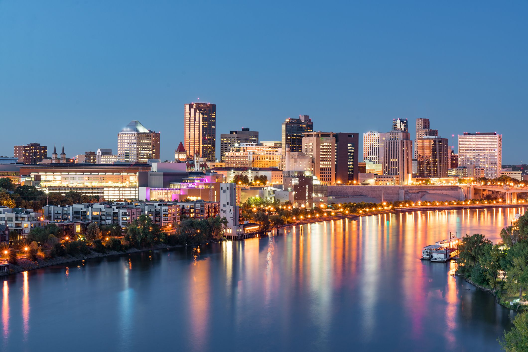 St. Paul, Minnesota skyline along the Mississippi River during evening, colorful lights, a boat in the river, a dark blue sky