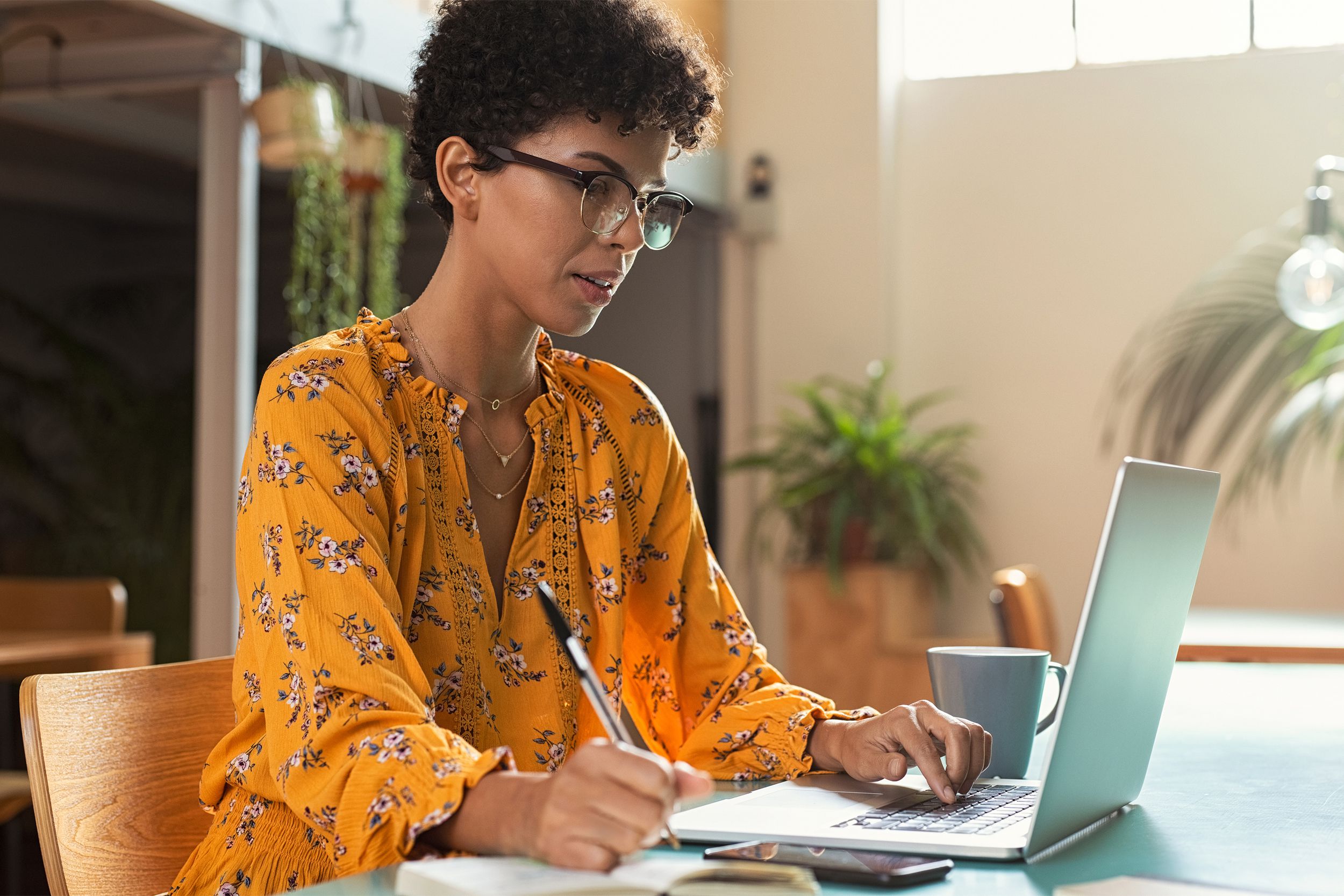 Woman on her laptop and writing notes in a notepad