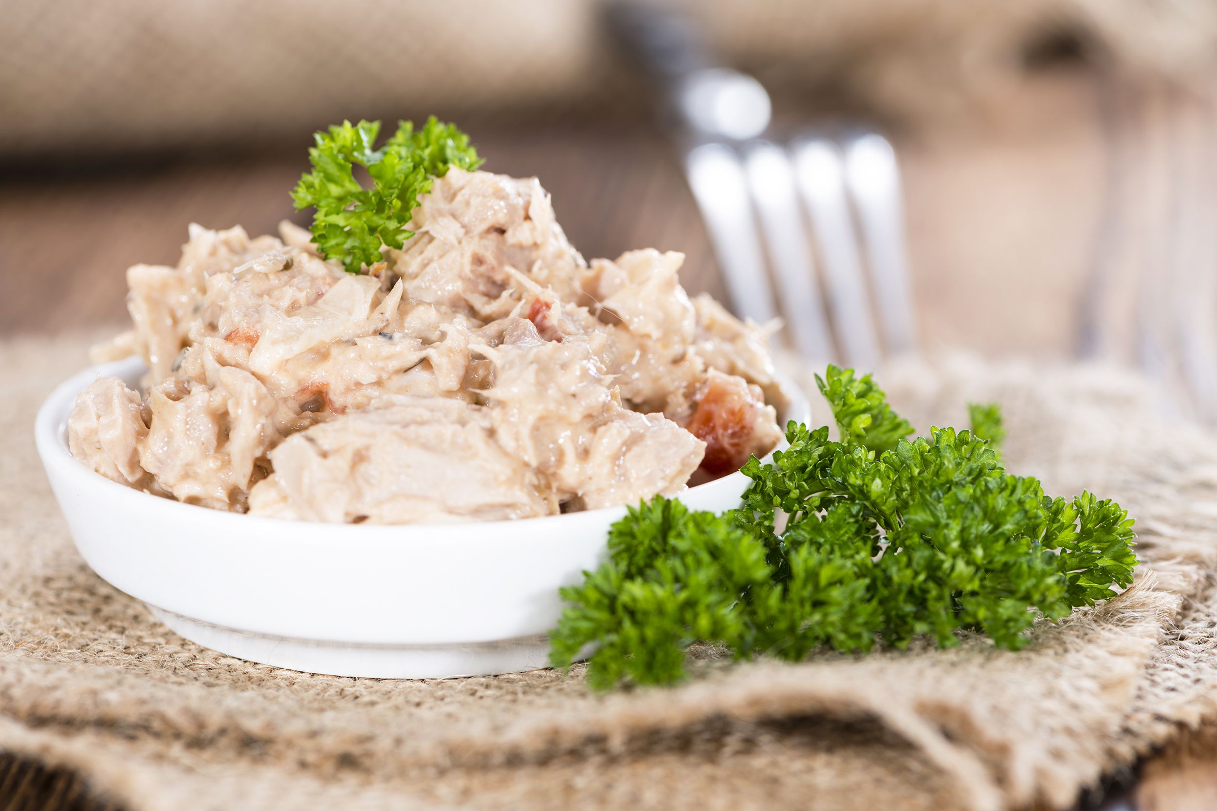 Tuna Salad in a white shallow bowl with a bunch of parsley on a beige cloth on a rustic wood table